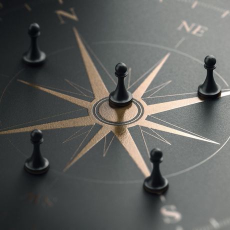 Black pawns on a gold and black compass, symbolizing strategic direction.