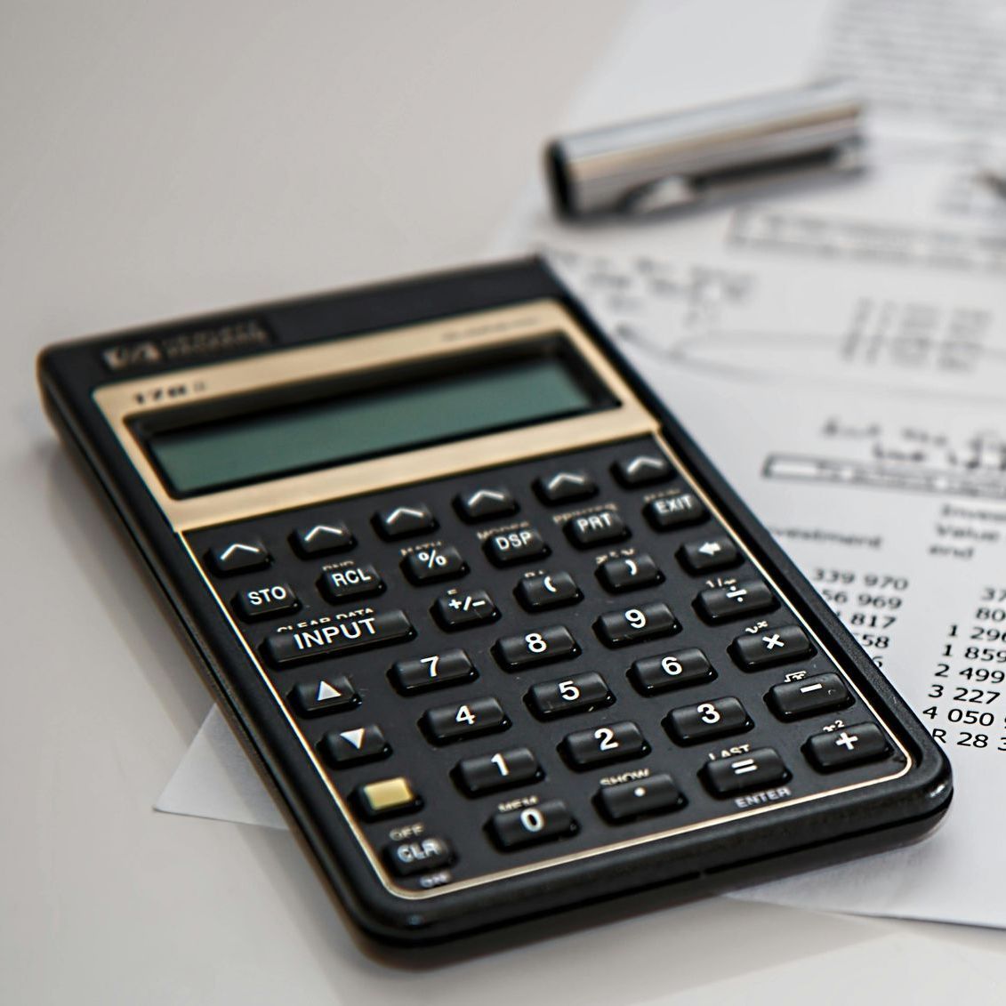 Black and gold calculator on a desk with papers and a pen.