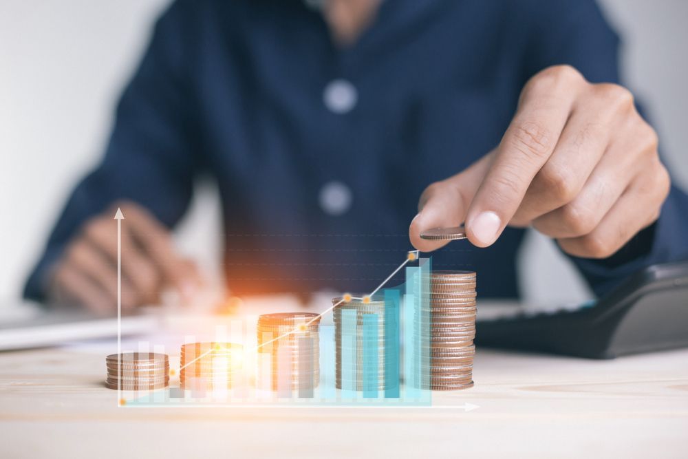 Person stacking coins with a growing financial chart overlay.