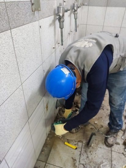 Persona con casco y chaleco reflectante trabaja en el suelo de baldosas de un baño.