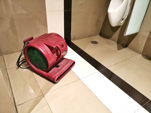 Red floor fan on tiled bathroom floor near a sink and shower area.