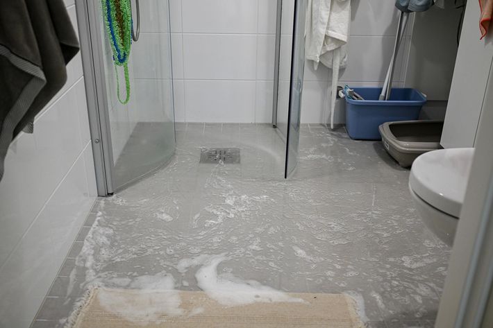 Small bathroom with a wet, white-covered floor and cleaning supplies visible in the corners.