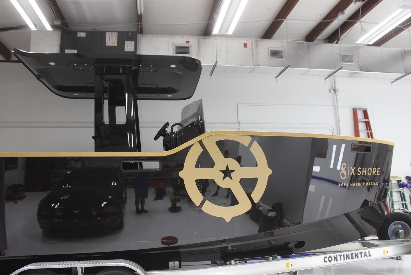Black car in a garage under a raised lift, with a gold gear logo on the glass panel.