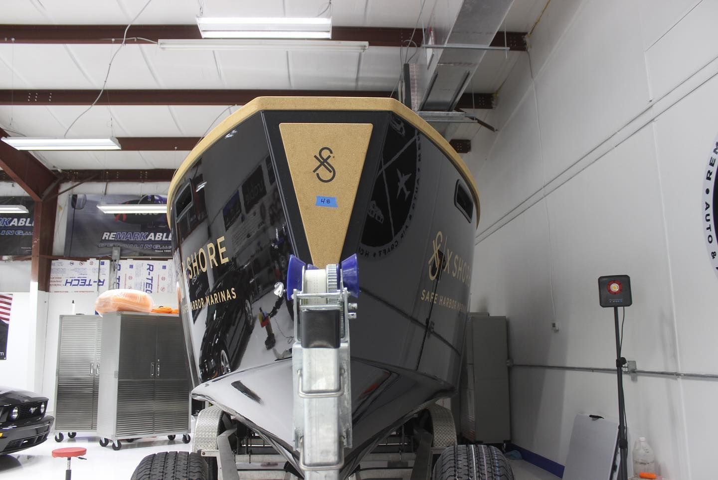 Black and gold boat in a garage, front view with storage bins and trailer jack visible