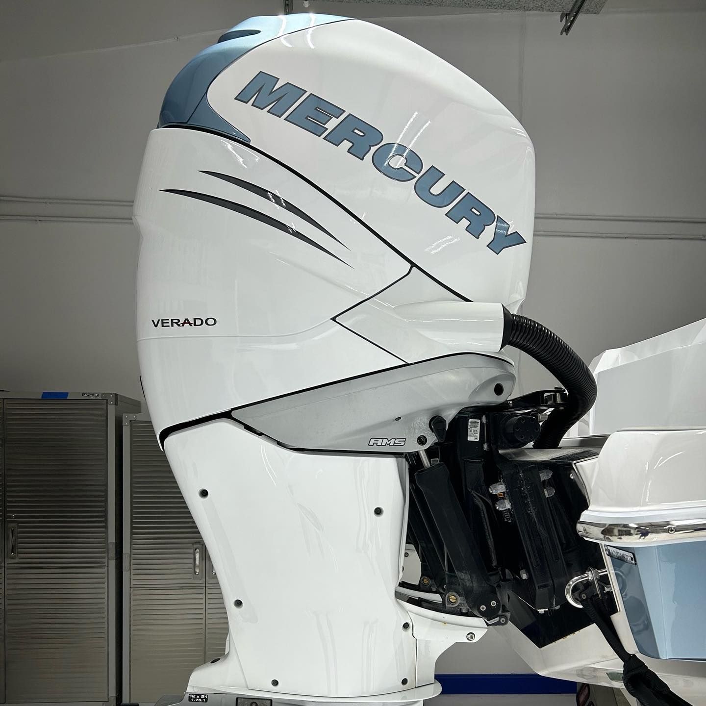 White Mercury Verado outboard boat motor with blue logo, mounted indoors on a vessel.