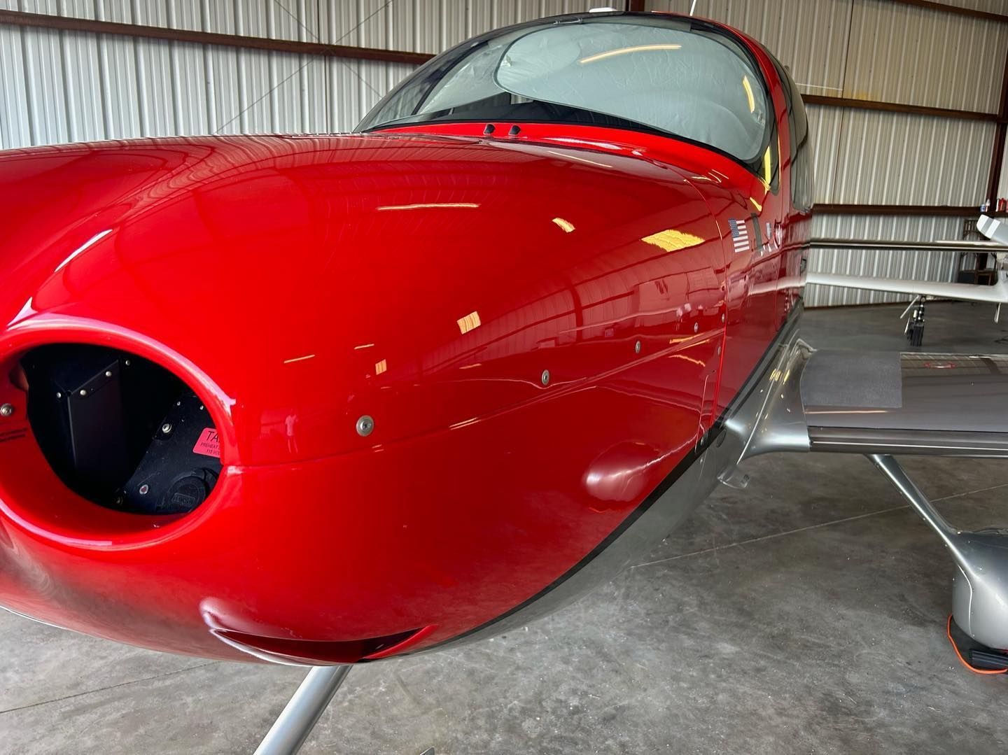 Red single-engine airplane nose in a hangar, with a glossy red fuselage and cockpit canopy visible