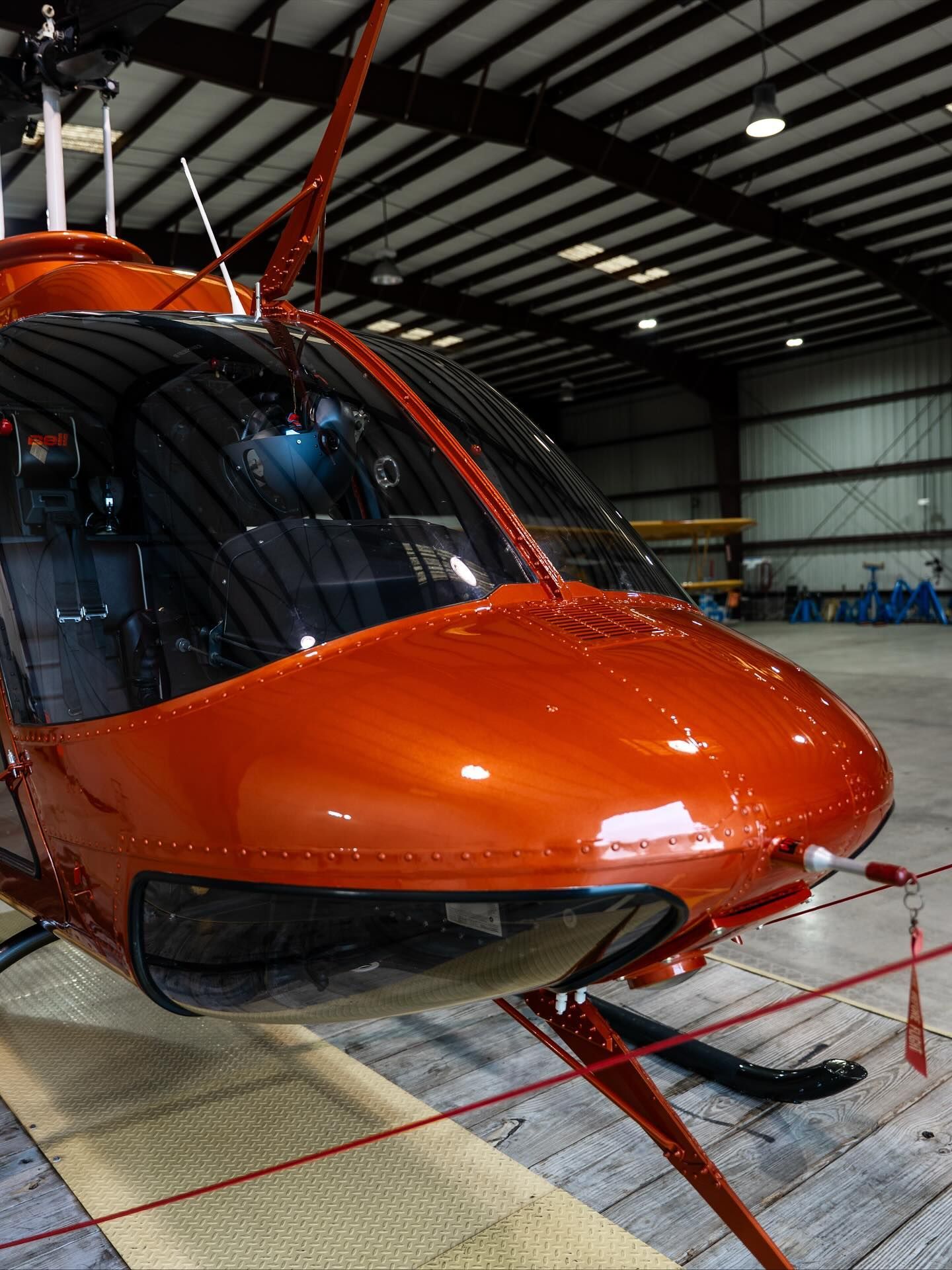 Orange helicopter nose inside a hangar, with red rotor blades and black cockpit windows.