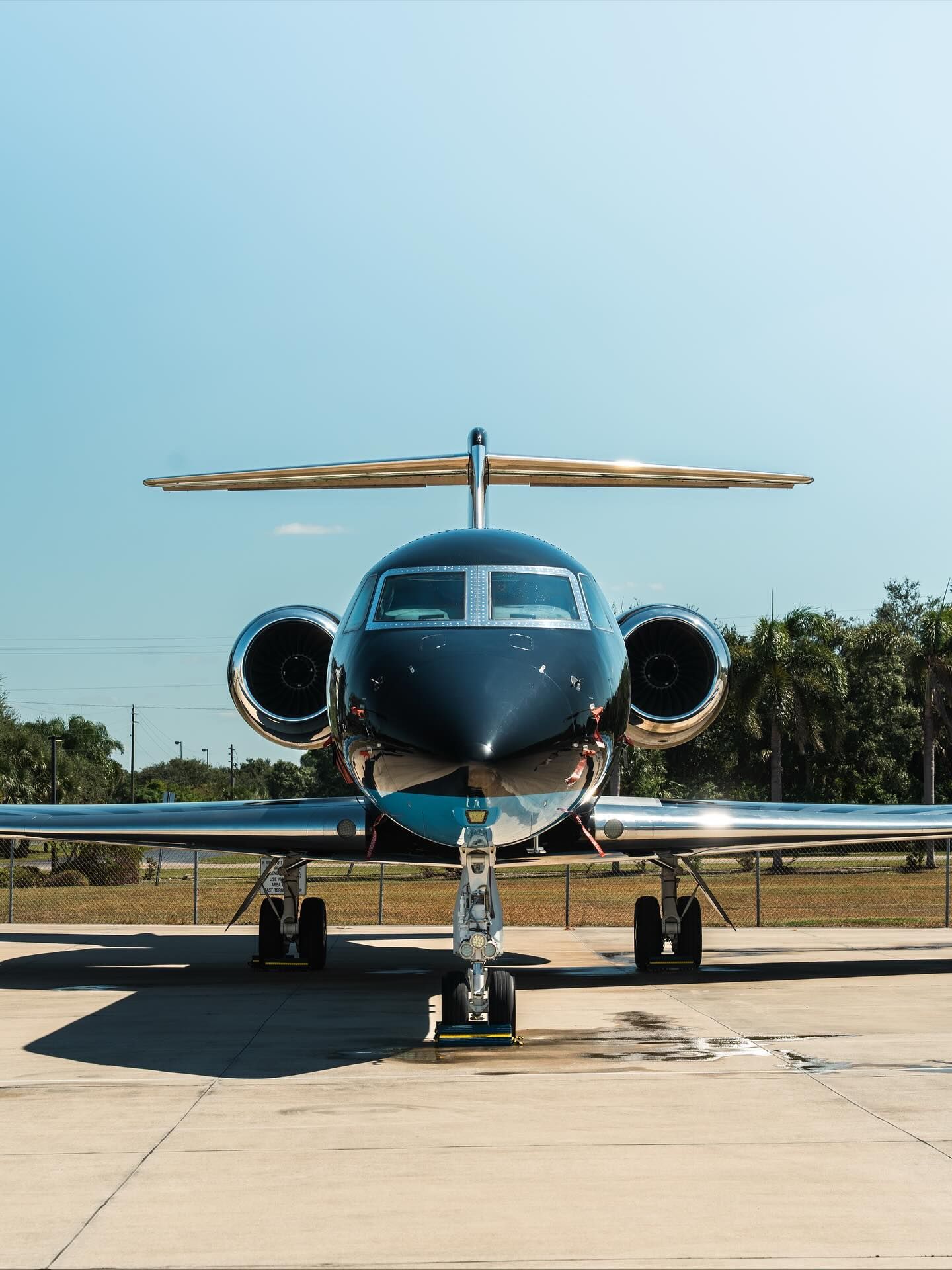 Front view of a dark blue private jet parked on a runway under a clear sky.