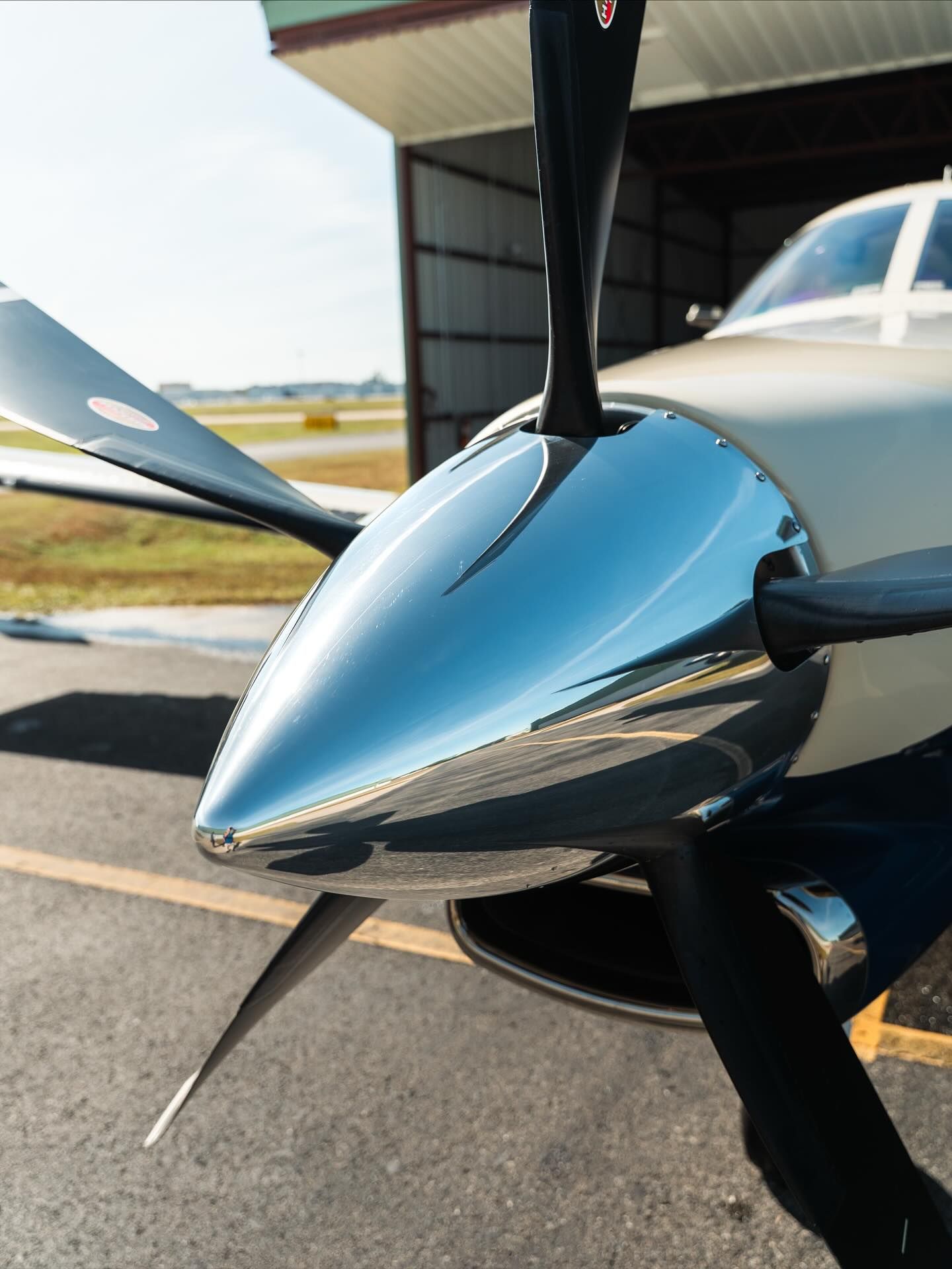 Close-up of a silver airplane propeller nose cone on a small aircraft at an airport hangar