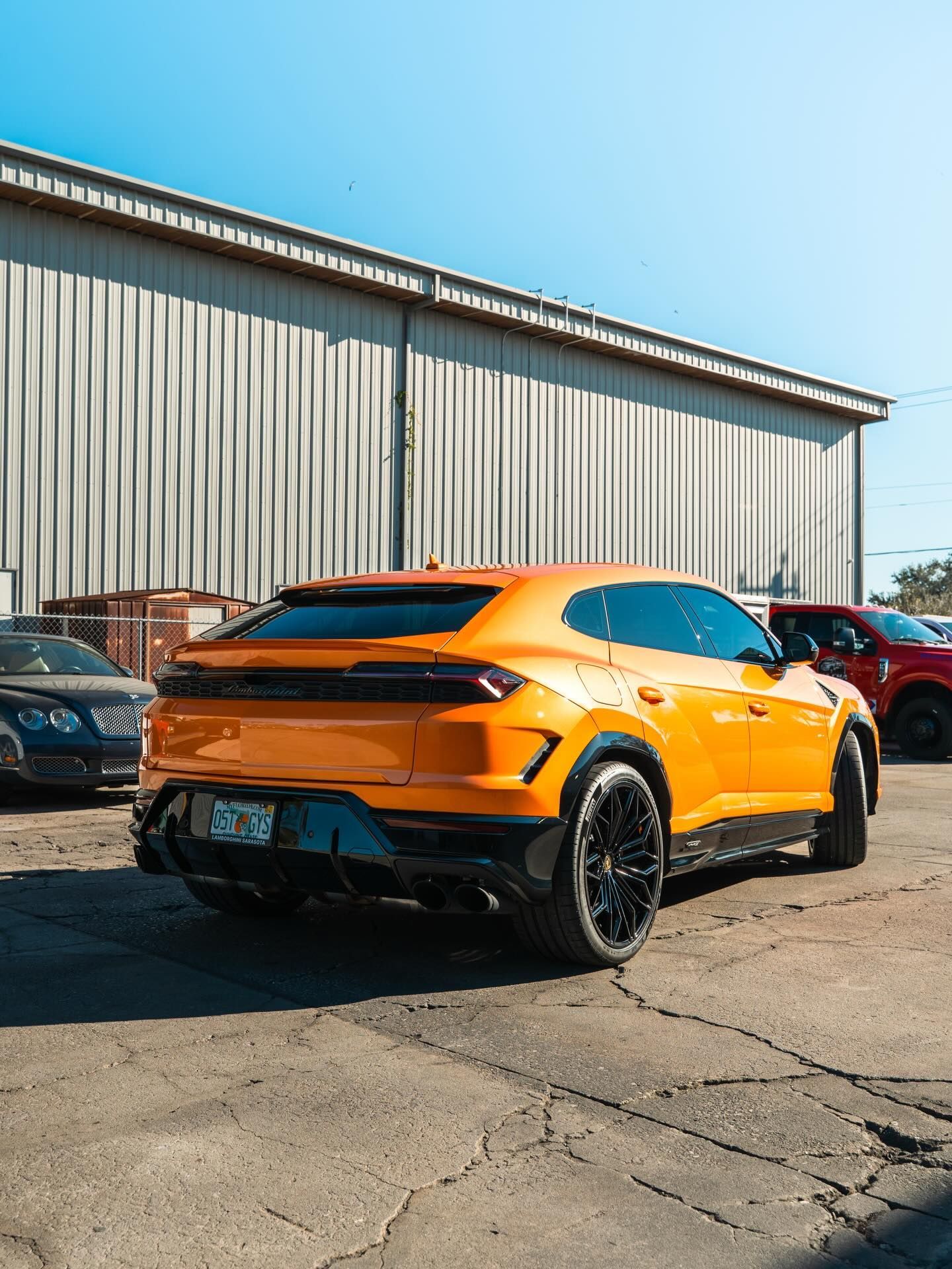 Orange sports car parked outside a metal warehouse on a sunny day