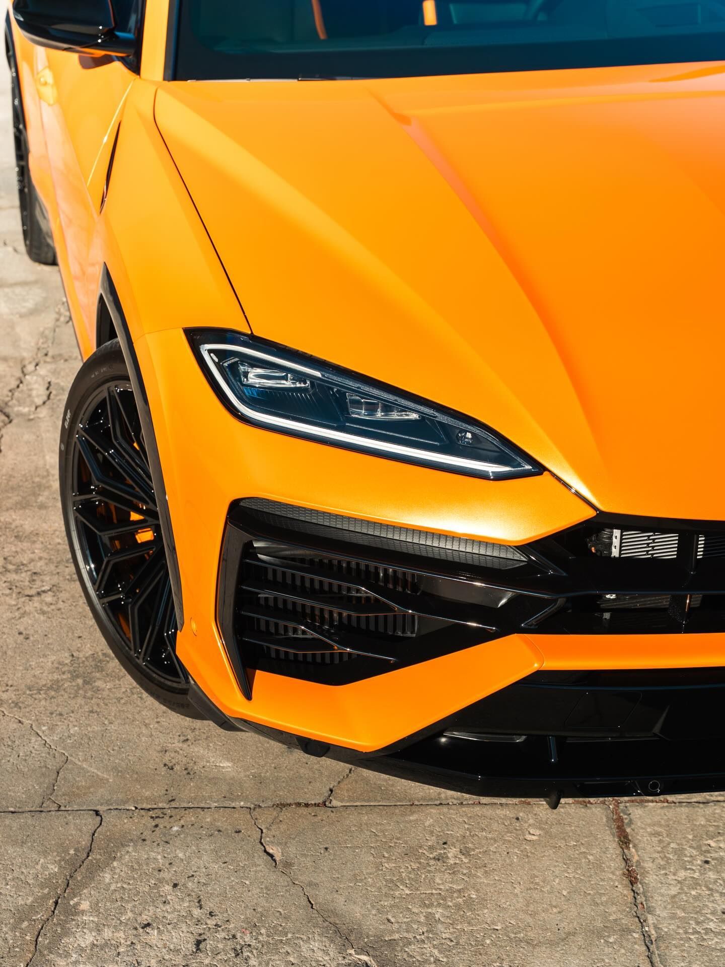 Close-up of an orange sports car’s front end with black rims on cracked pavement