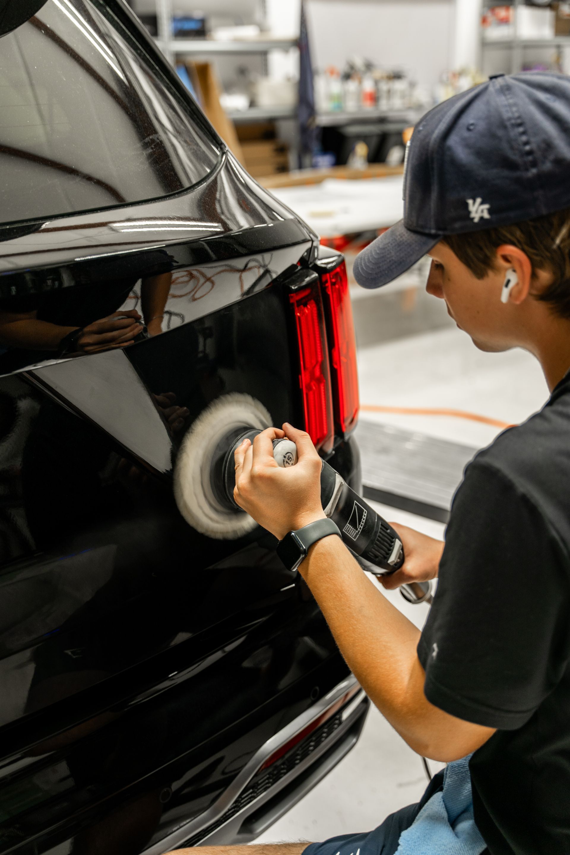 Detailing a black SUV’s rear light with a polishing tool in a workshop