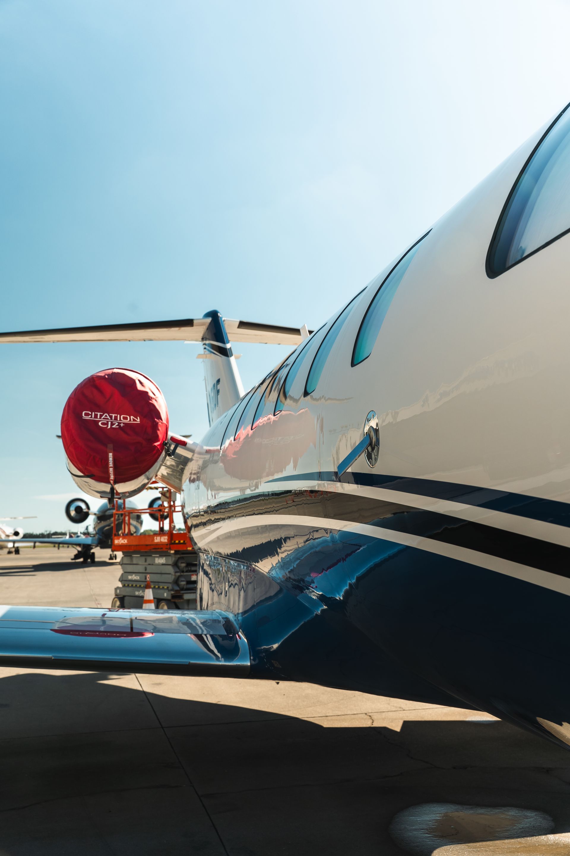 Private jet on tarmac with red engine cover, viewed from the side under a clear blue sky