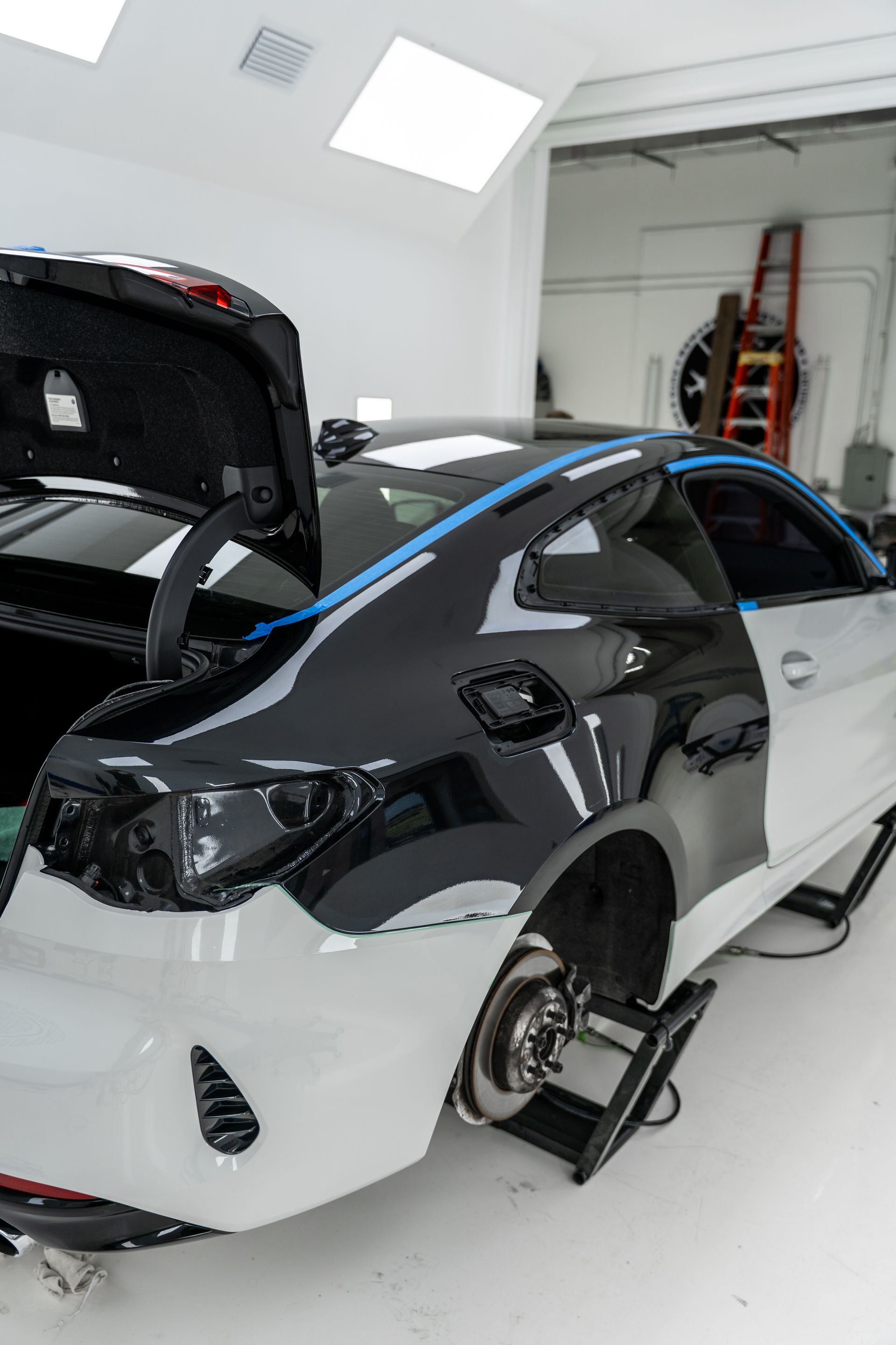 White and black car in a repair shop with the rear bumper removed and the trunk open