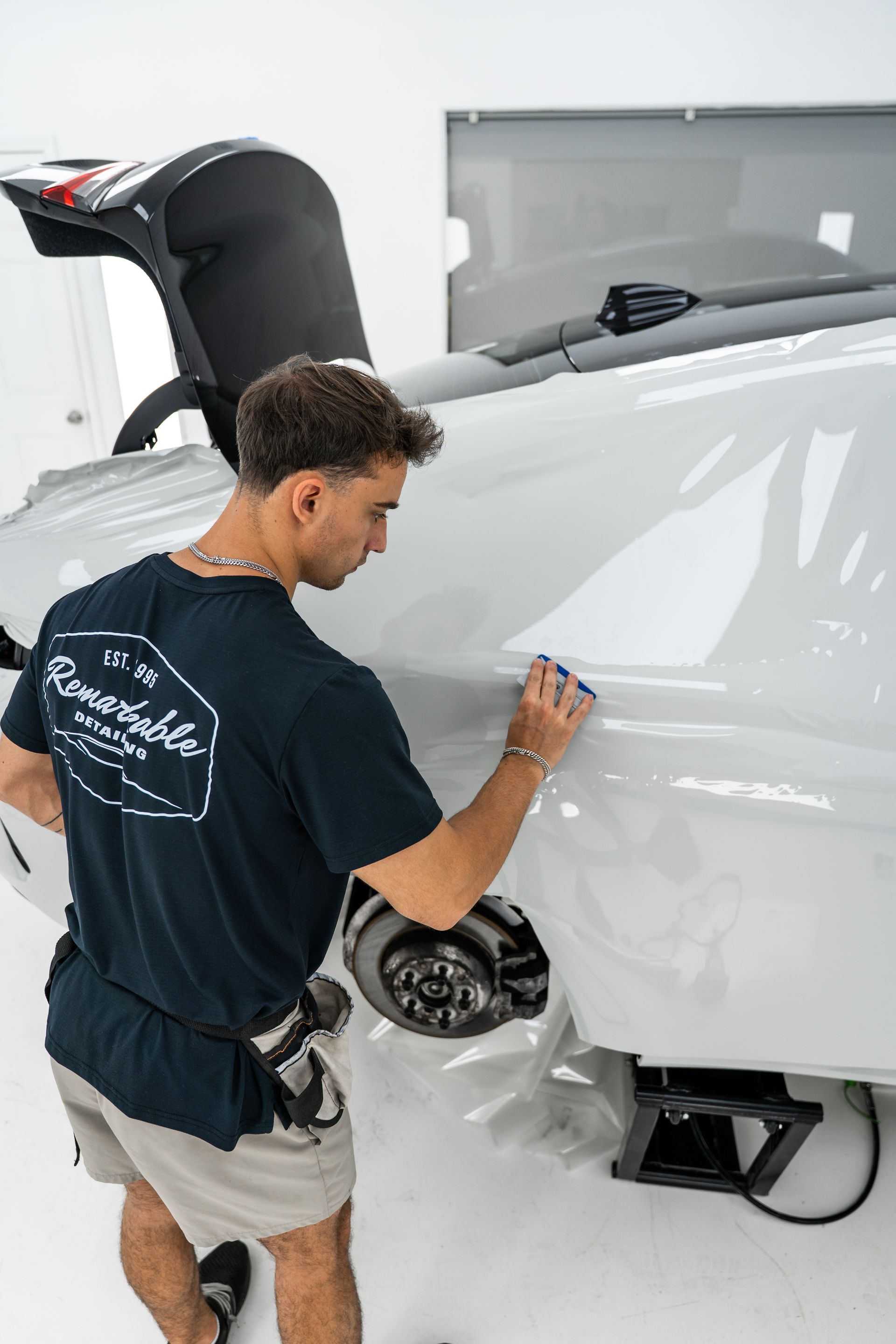 Man polishing the rear side of a white car in a garage