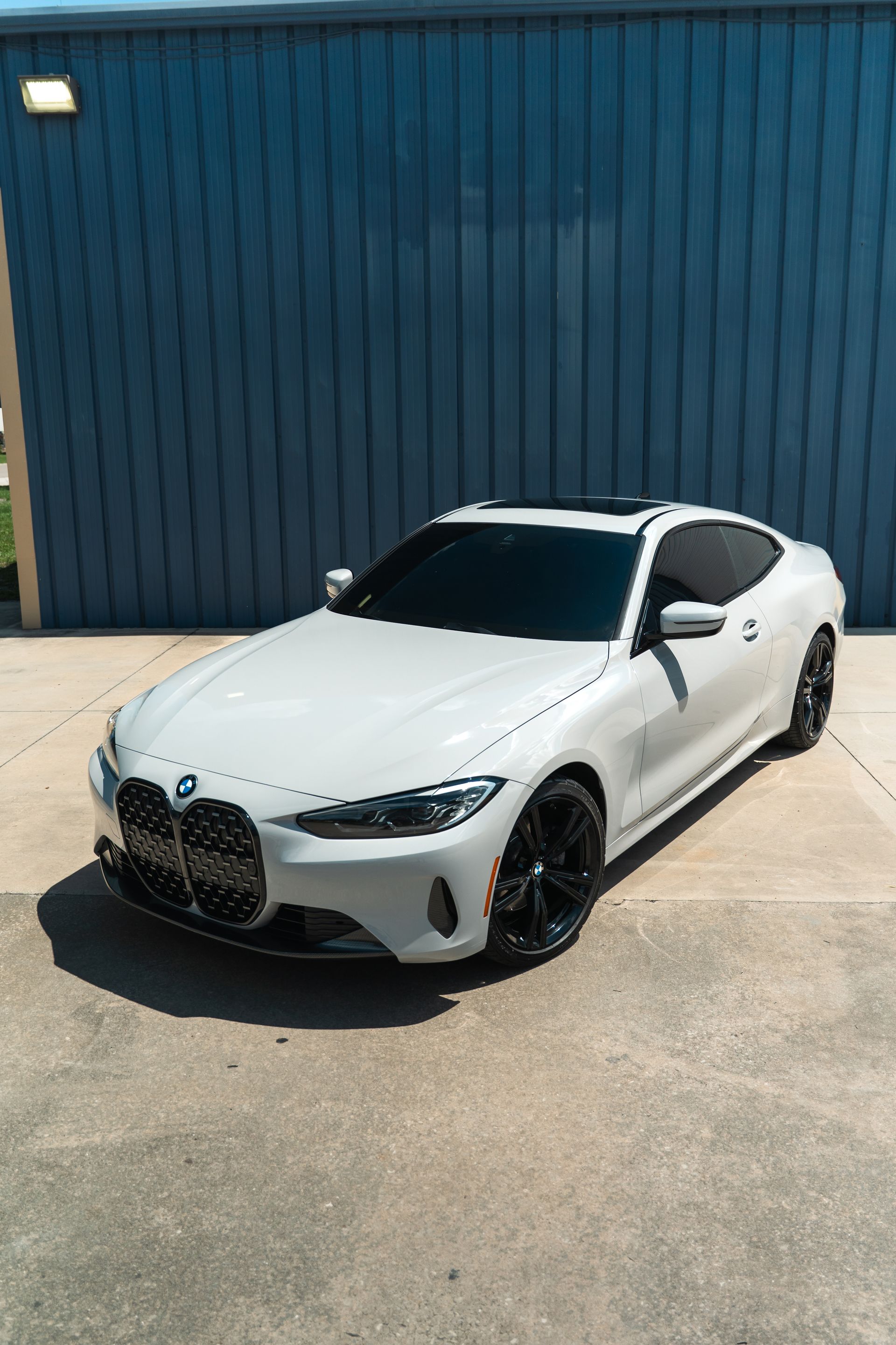 White BMW parked in front of a blue corrugated metal building.