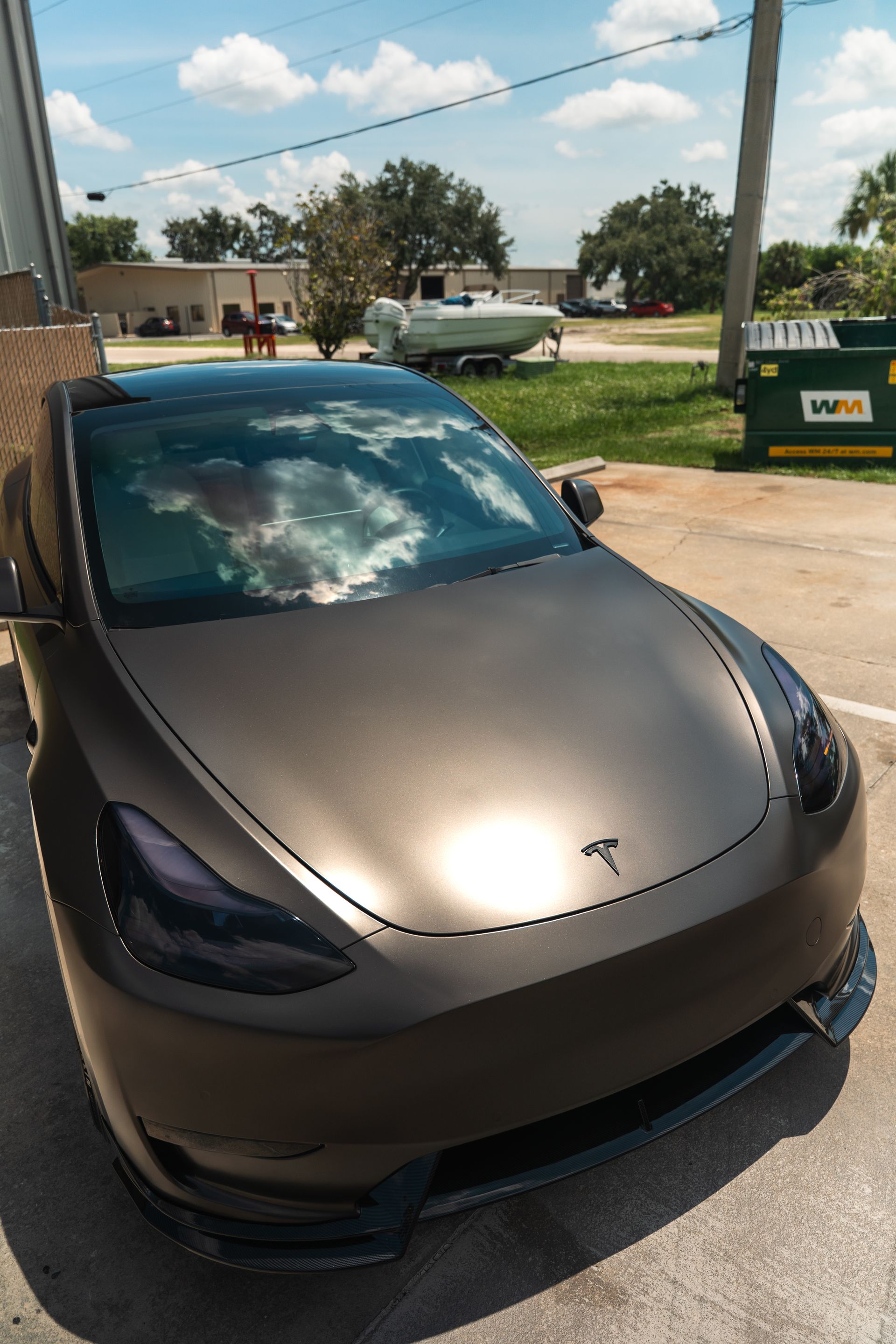 Matte brown Tesla parked outdoors under a partly cloudy sky