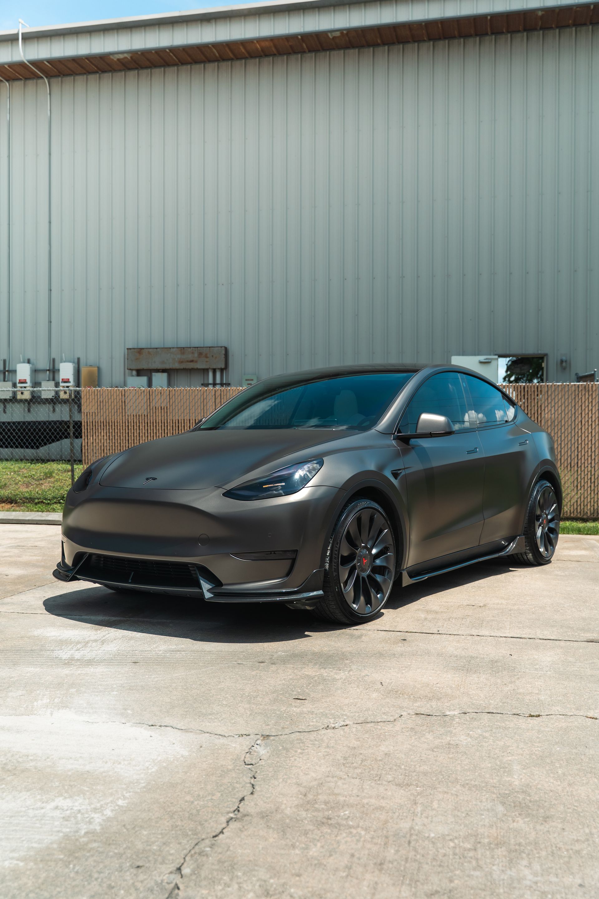 Dark gray Tesla parked outside an industrial building on a concrete lot