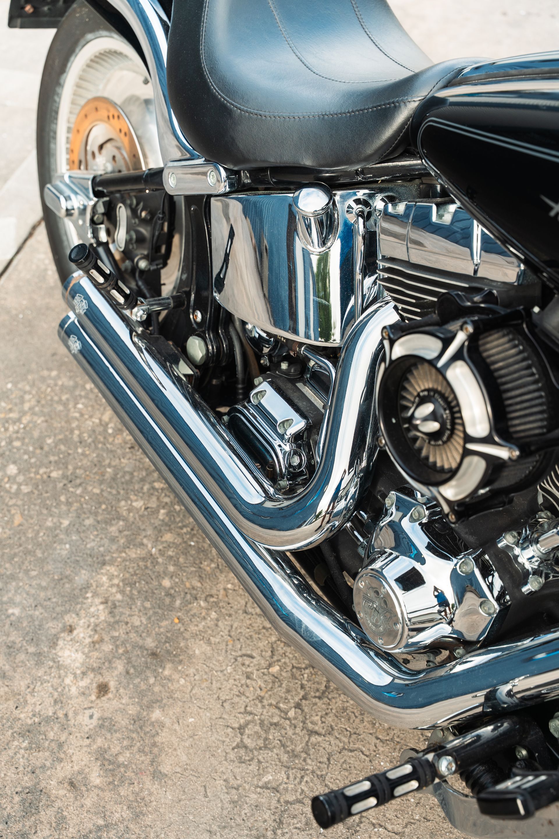 Chrome motorcycle engine and exhaust with black bodywork and rear wheel detail.