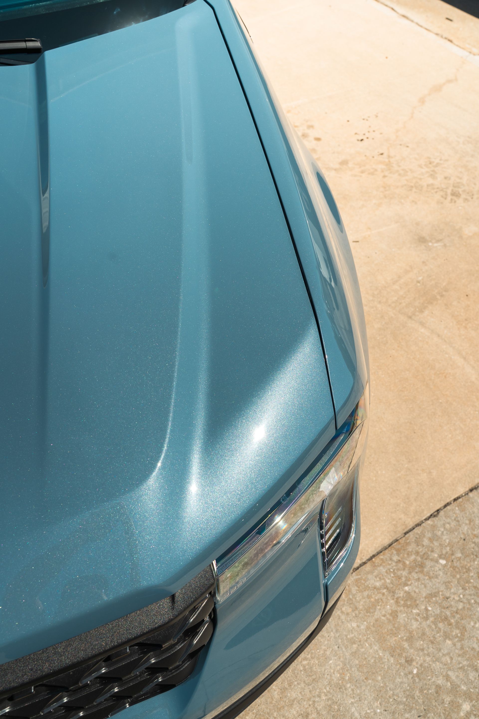 Close-up of a teal car’s front corner parked on a driveway.