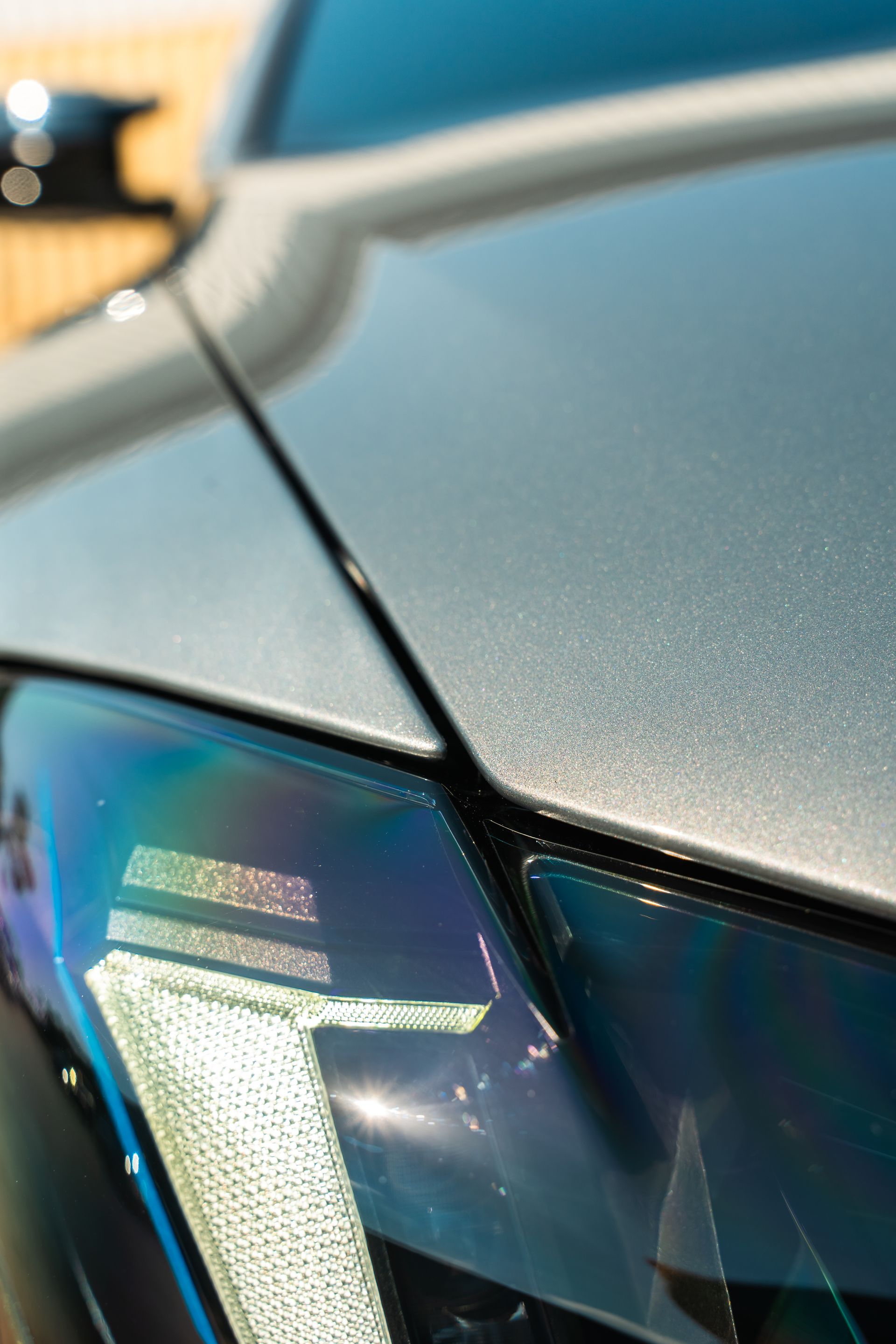 Close-up of a silver sports car hood and headlight with metallic blue reflections