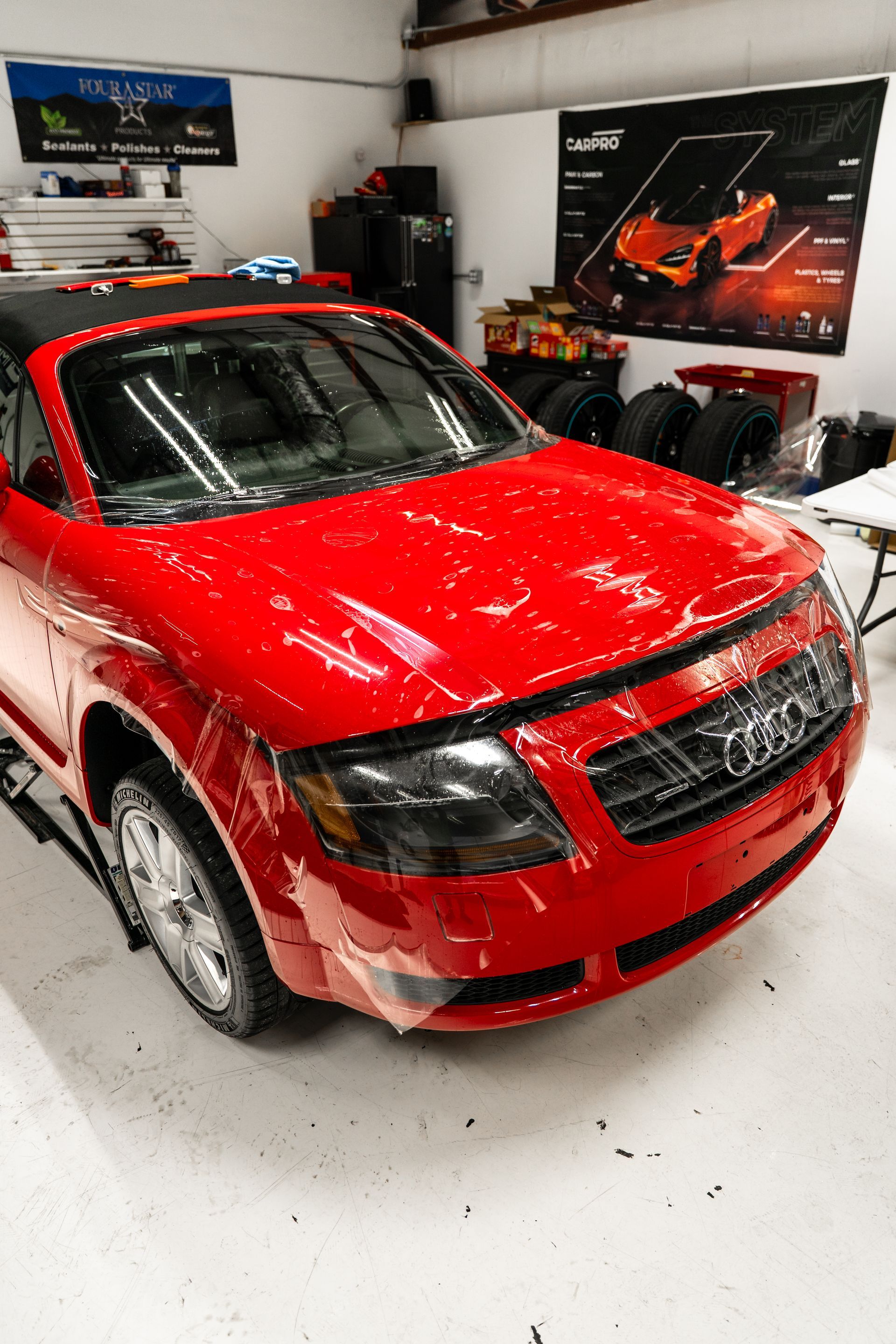 Red car in an indoor showroom, covered with confetti, with posters and equipment in the background