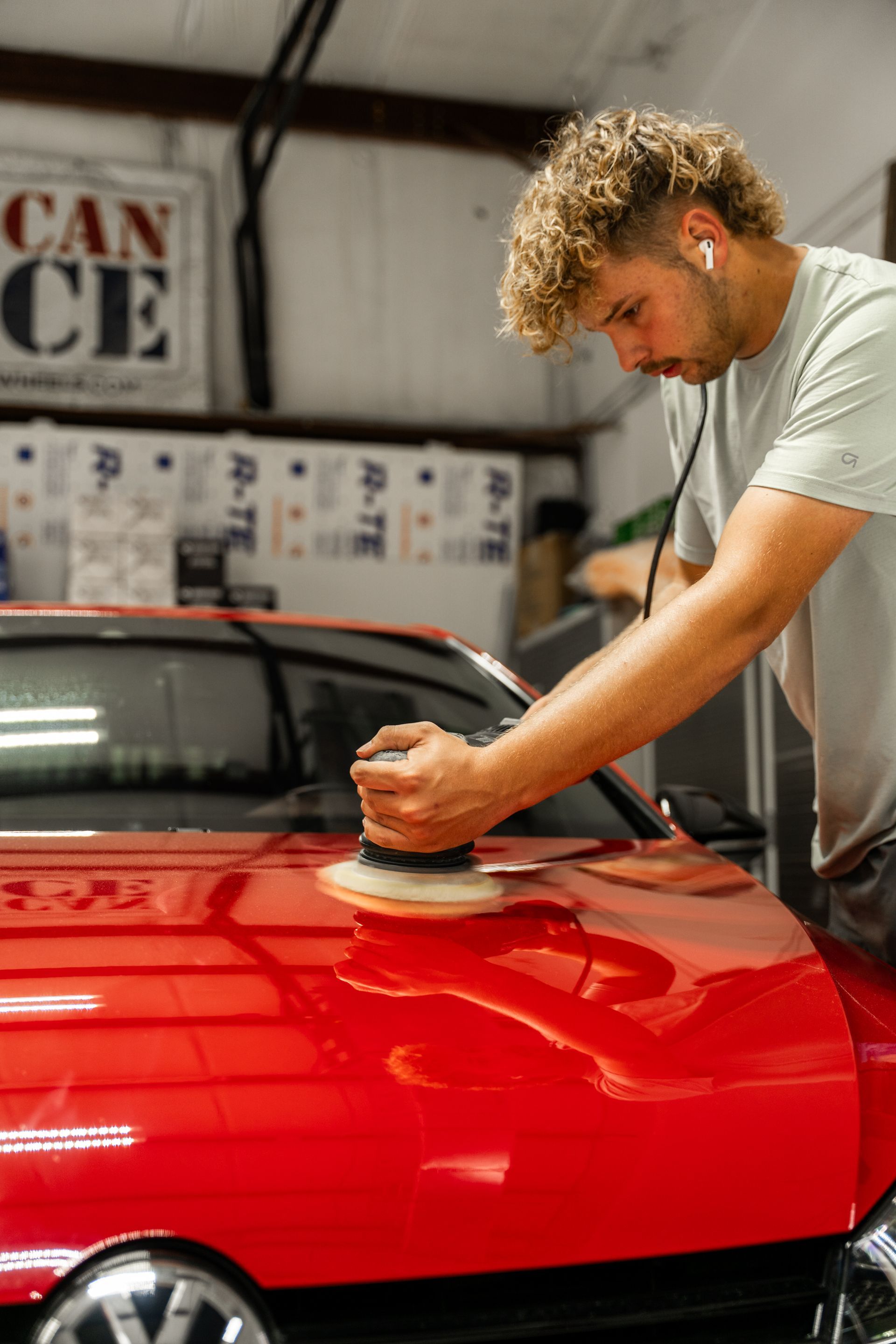 Man polishing a red car hood with a buffer in a garage