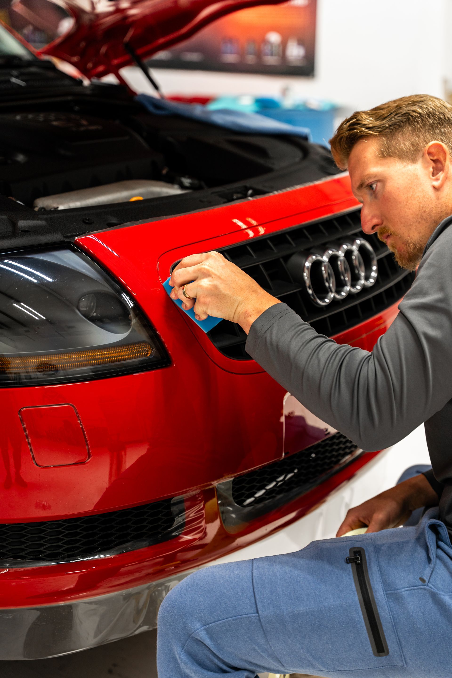 Mechanic polishing the front grille of a red Audi sports car in a garage