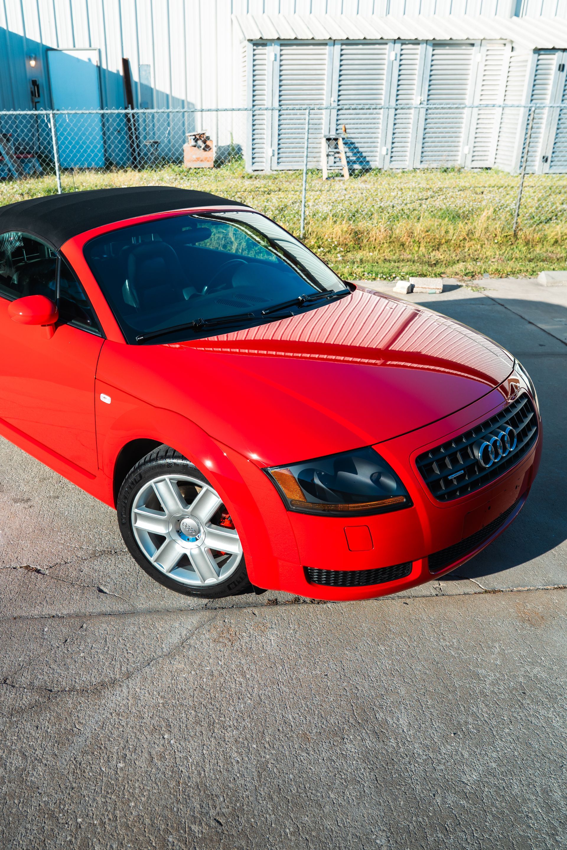Red Audi convertible parked outdoors beside an industrial building.