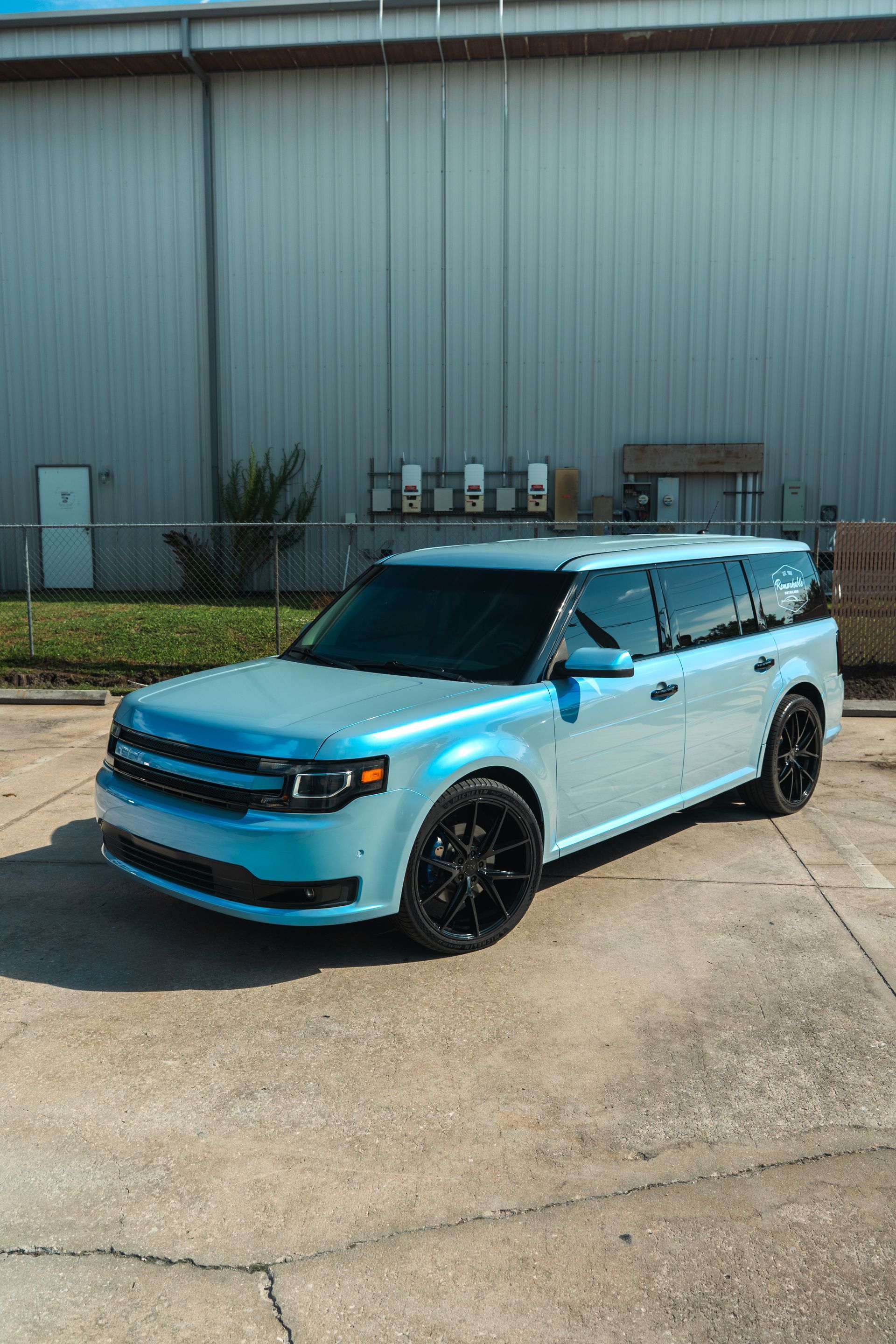 Blue SUV parked on a concrete lot beside a gray industrial building