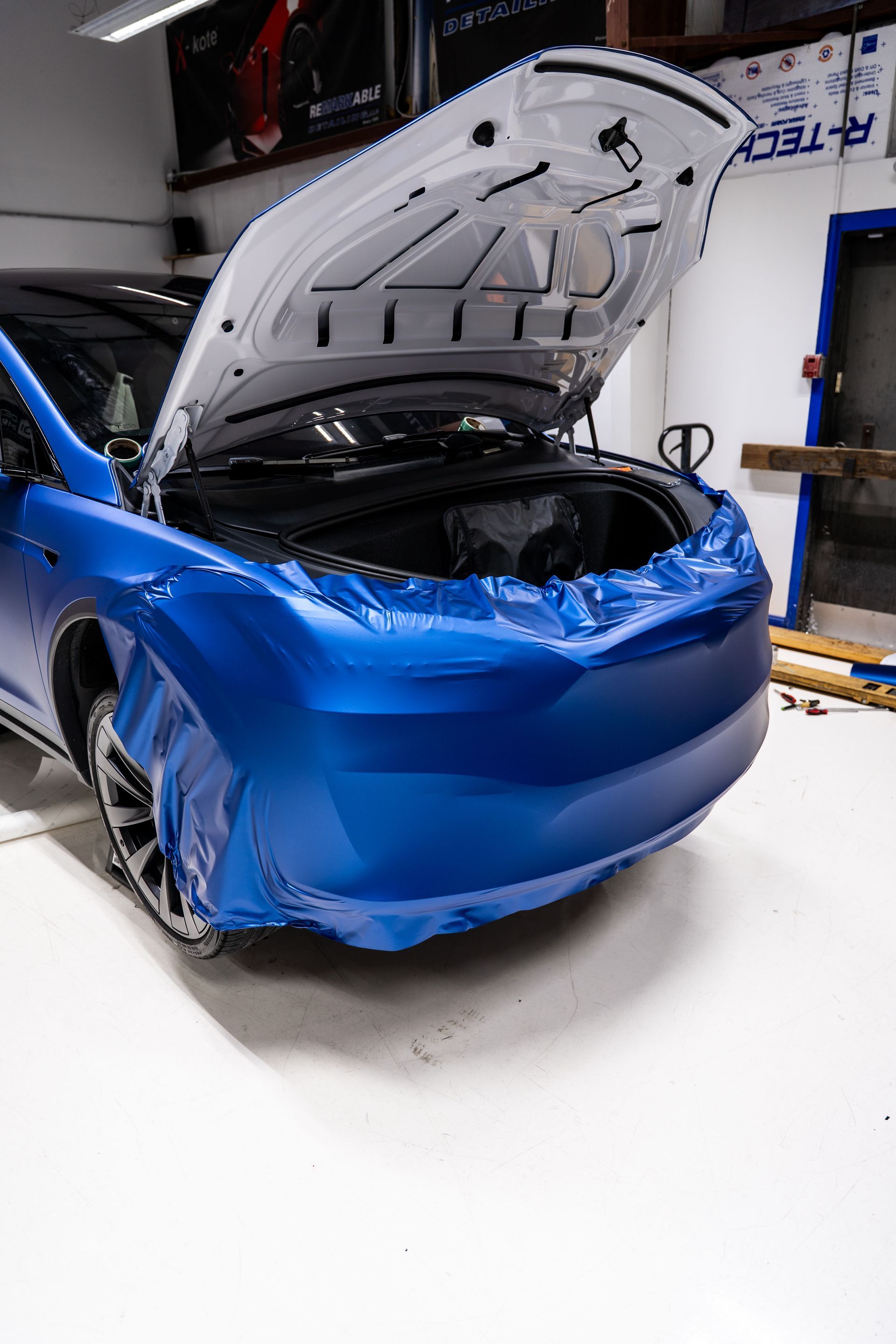 Blue car with crushed front end and open hood in an auto repair shop