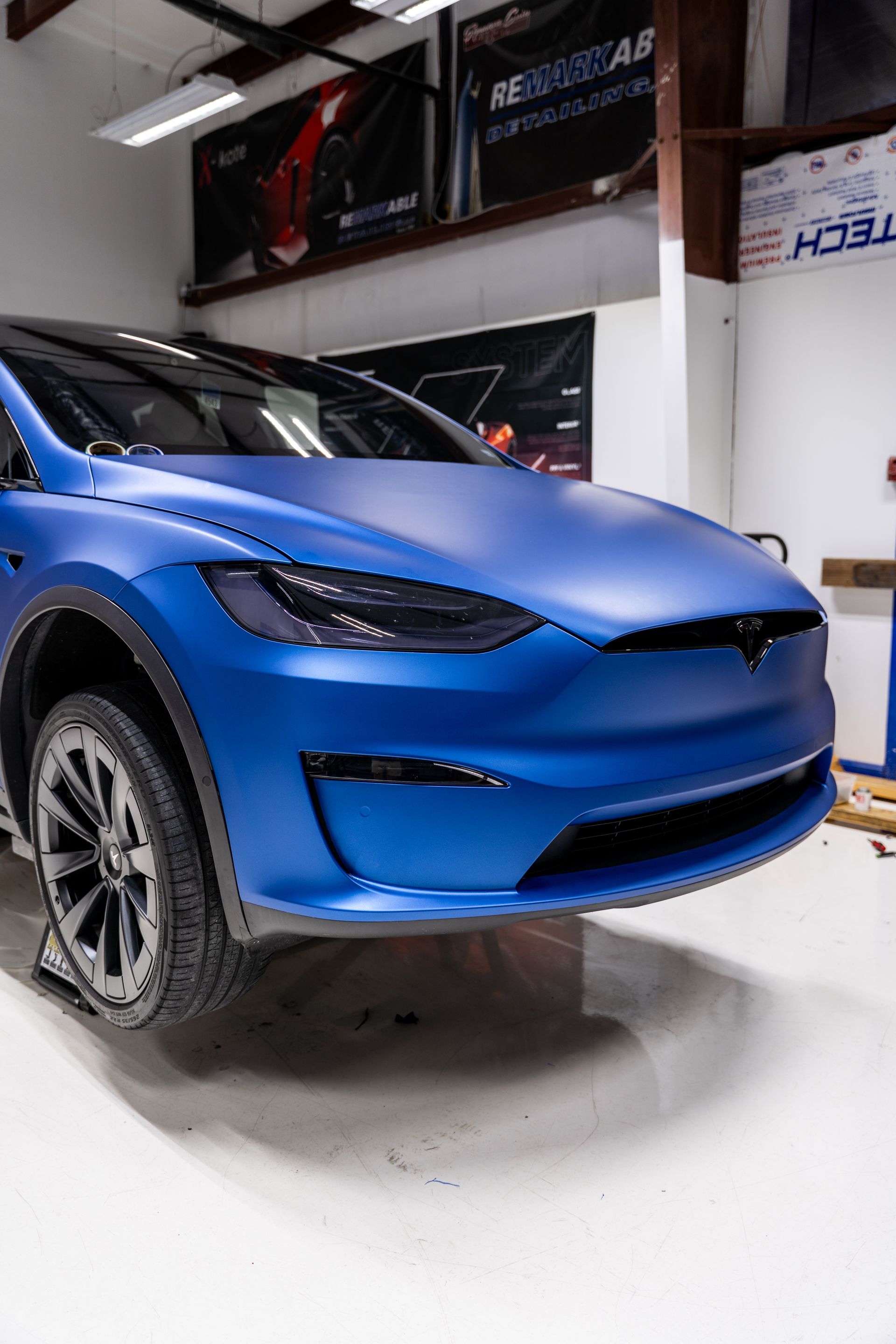 Blue electric SUV in a showroom, front view on a white floor with a wall banner in the background