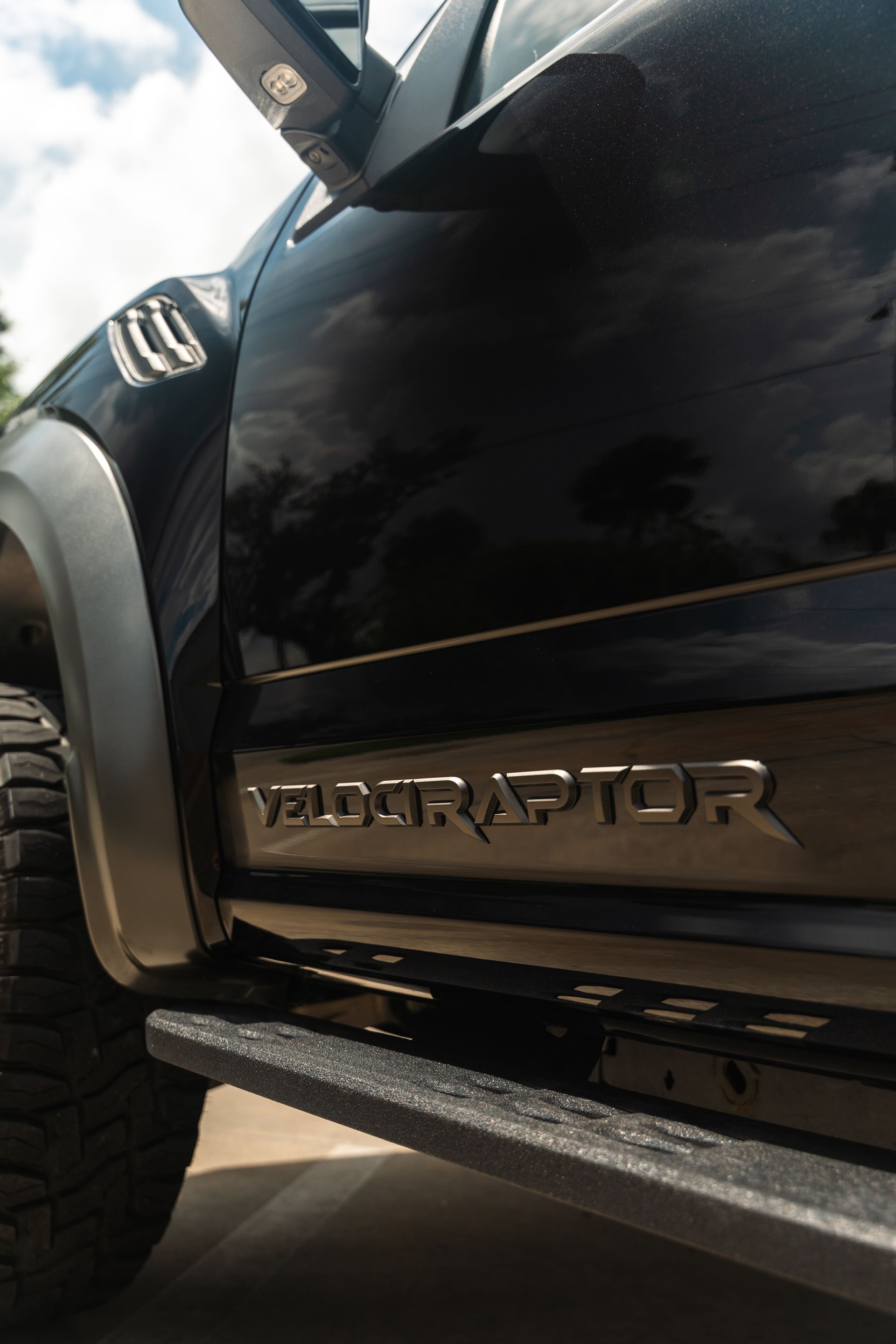 Black Ford Raptor truck side panel with VELARO/“VELO...” badge and off-road tire, low-angle view