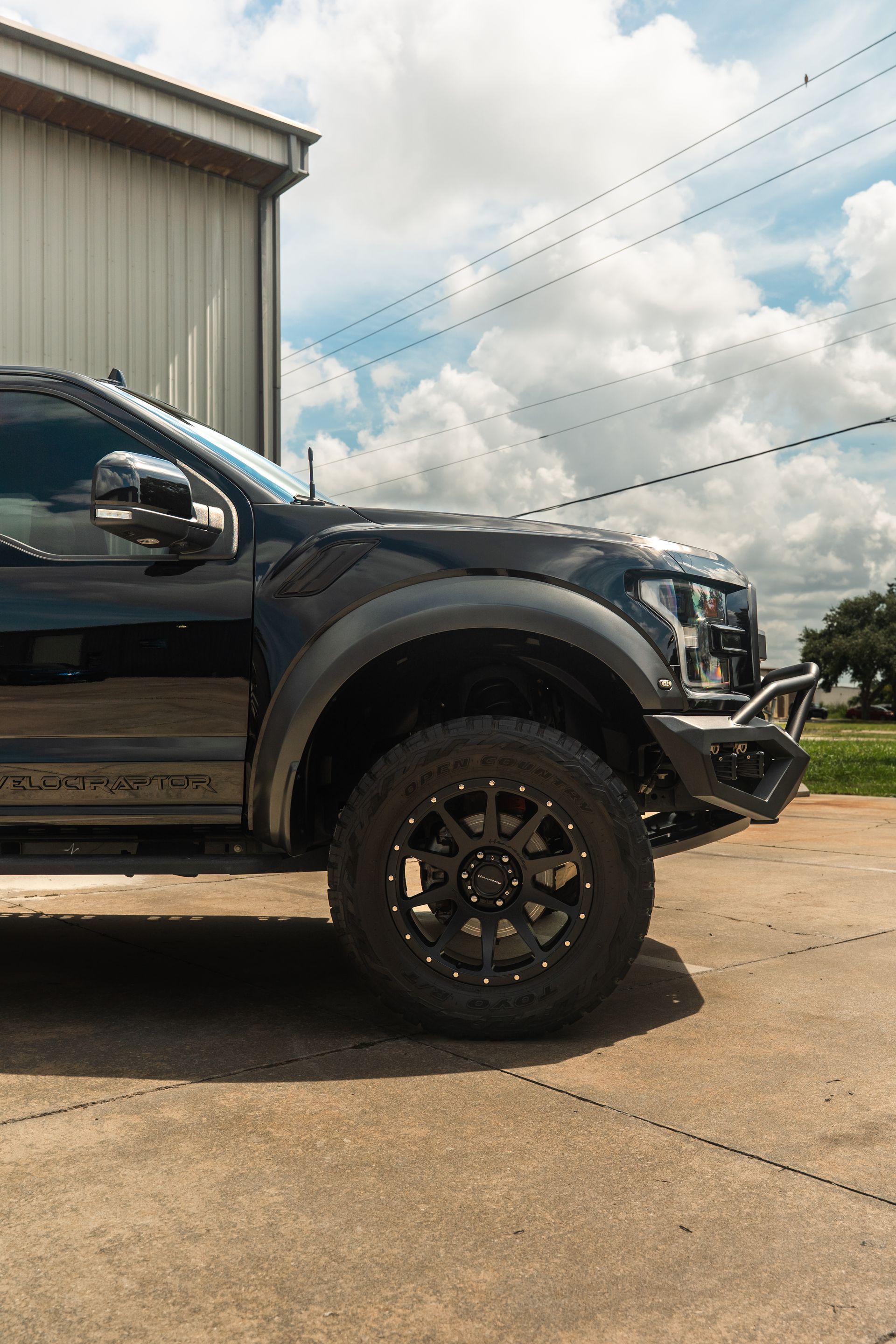 Black lifted pickup truck parked beside a building under a cloudy sky