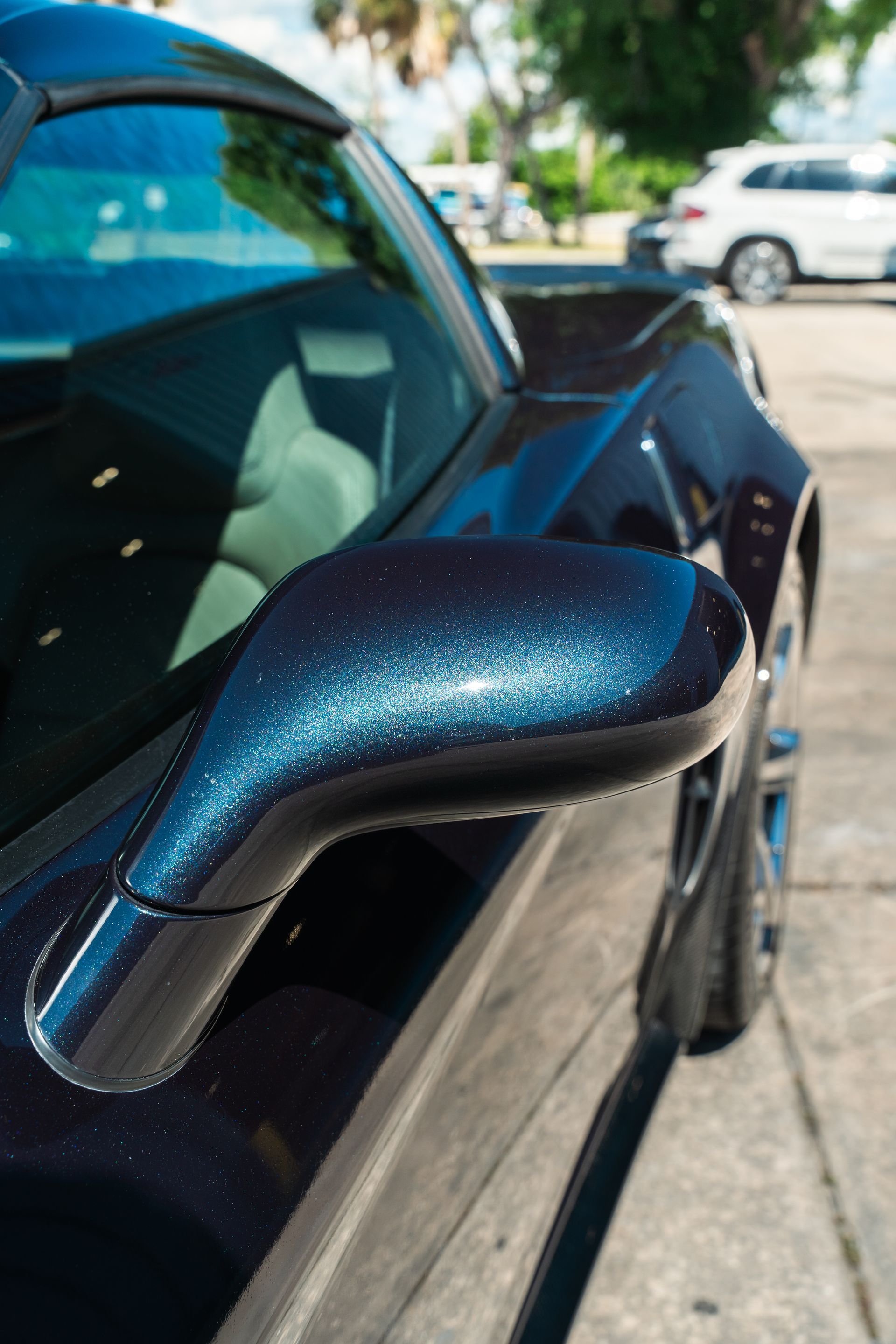 Close-up of a metallic blue car side mirror parked outdoors in bright sunlight