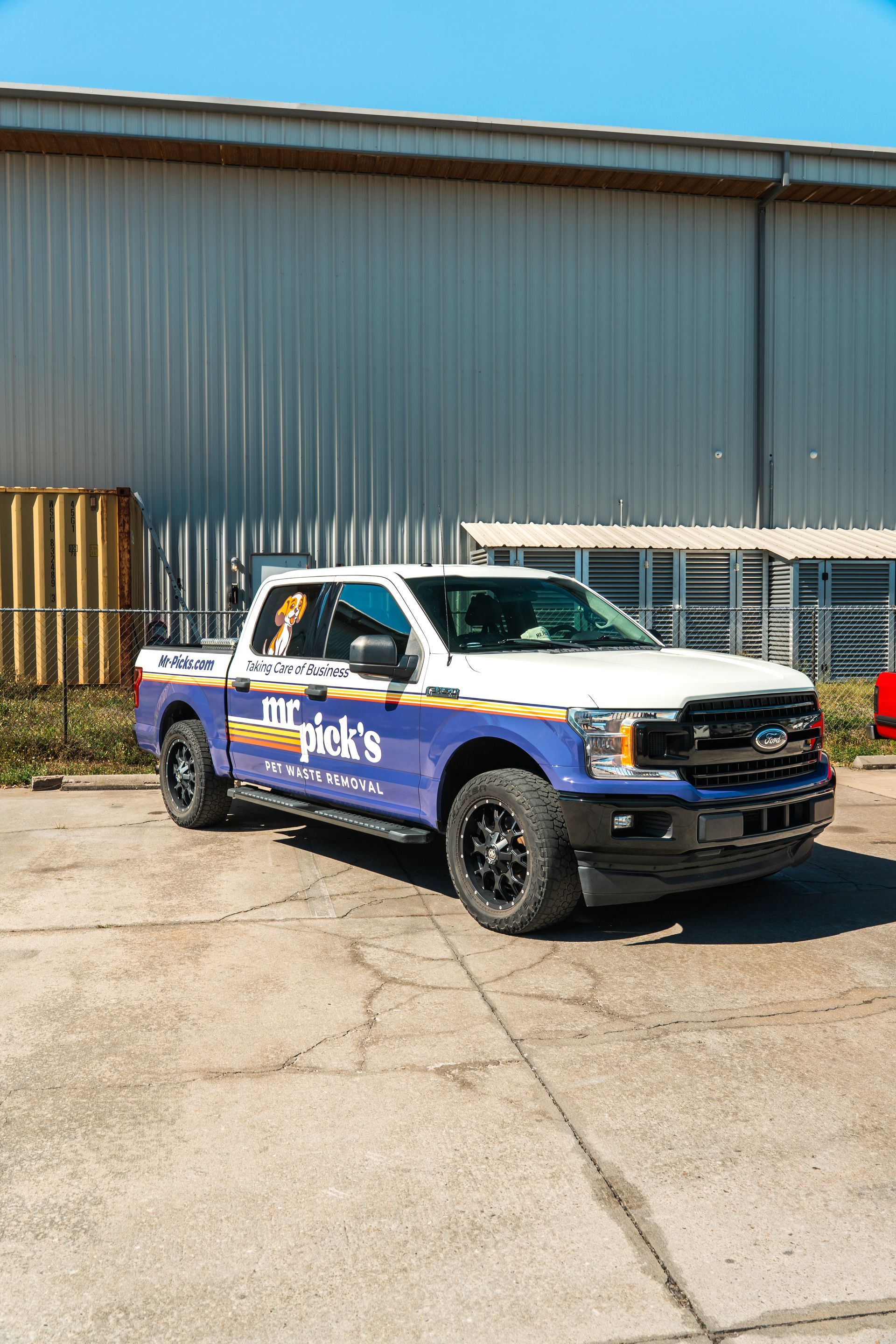 Blue and white pickup truck parked outside a warehouse on a sunny day