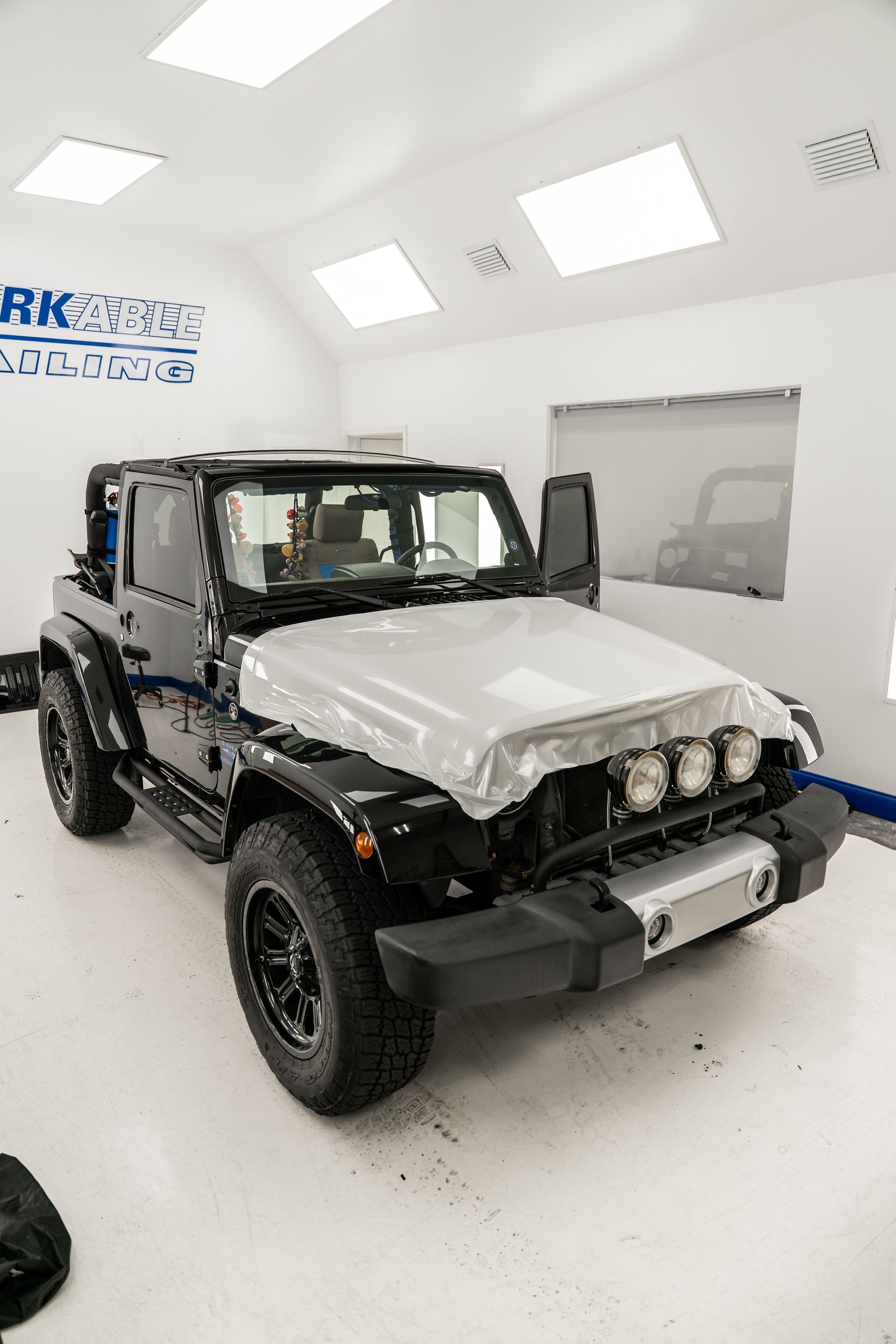 Black Jeep with exposed front end in a bright auto body shop