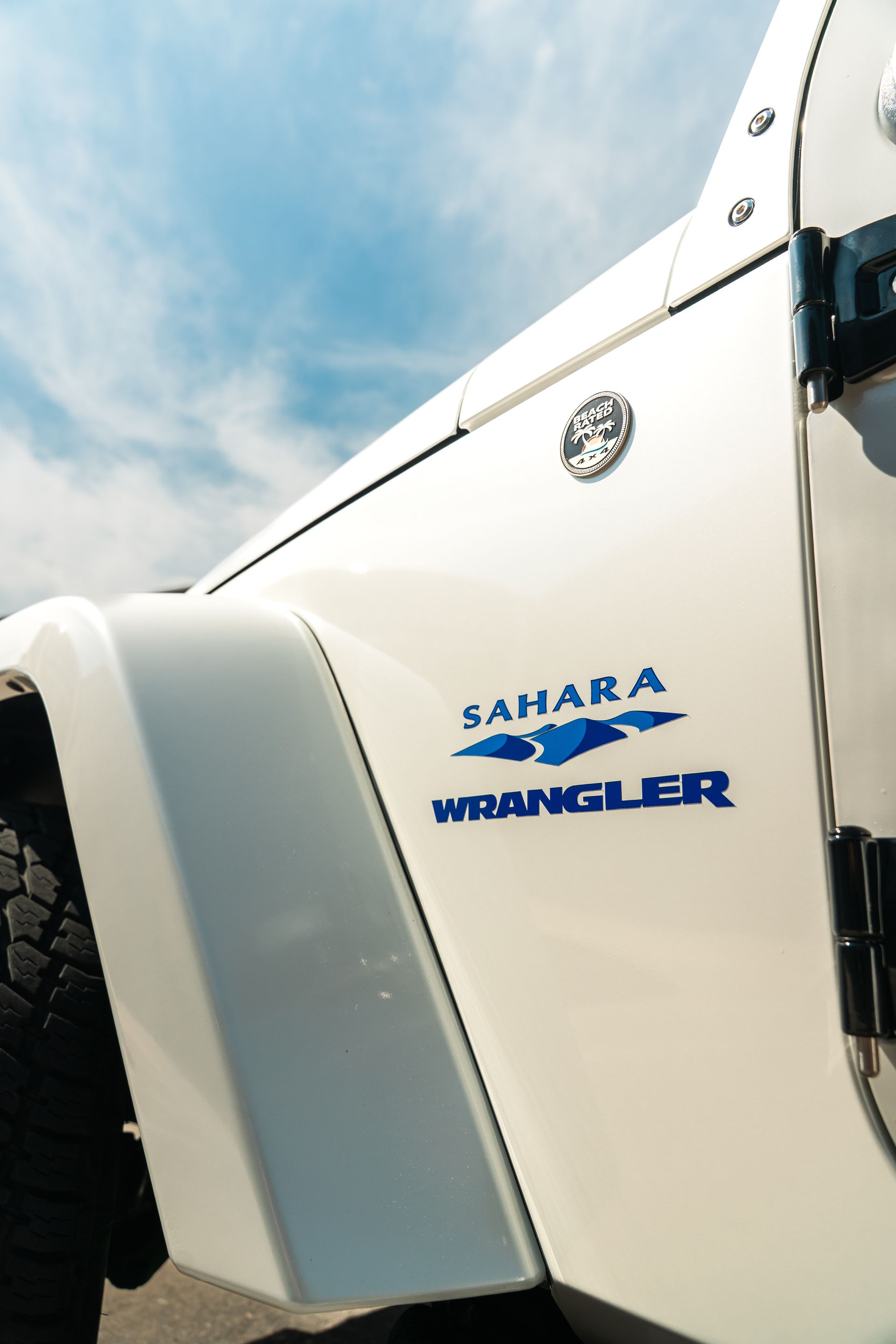 White Jeep Wrangler Sahara close-up with blue logo on the side against a cloudy sky