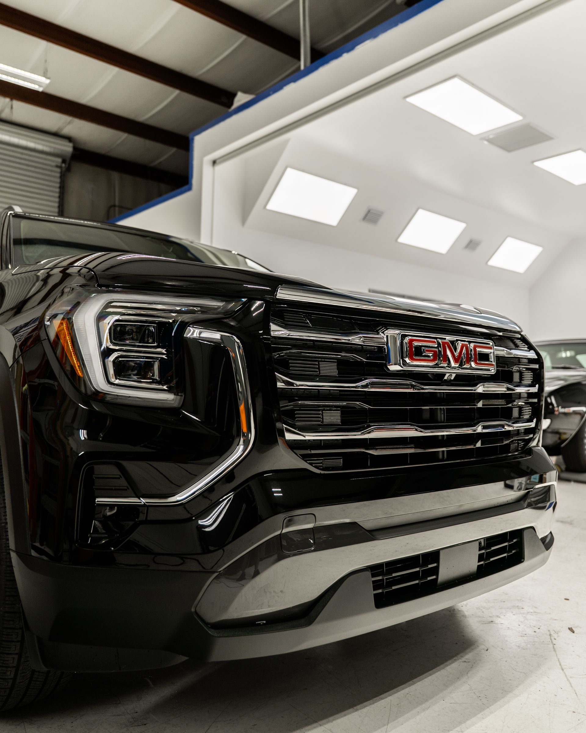 Black GMC truck front in a bright showroom, close-up of the grille and headlights