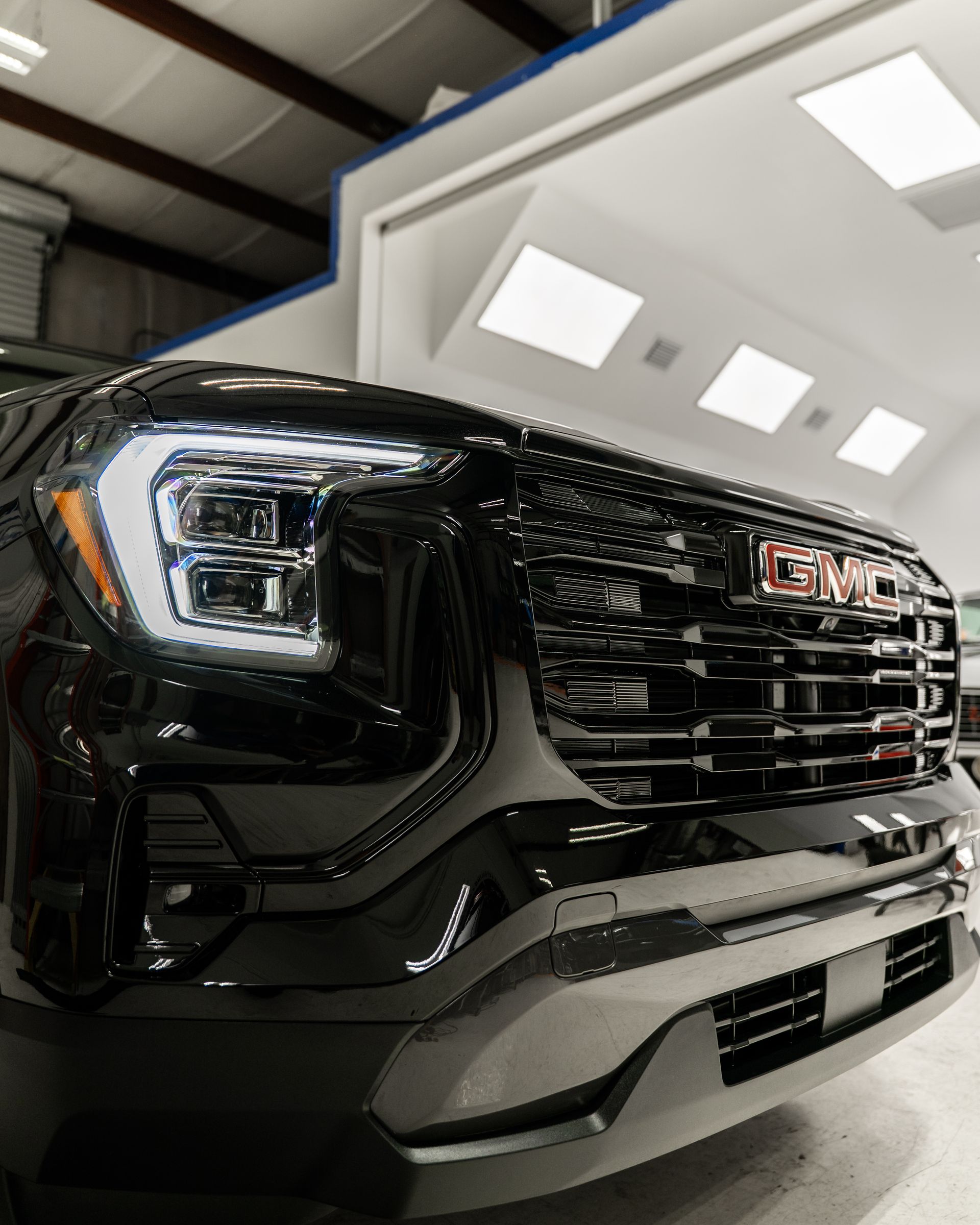 Black GMC truck front grille and headlight in a bright indoor showroom