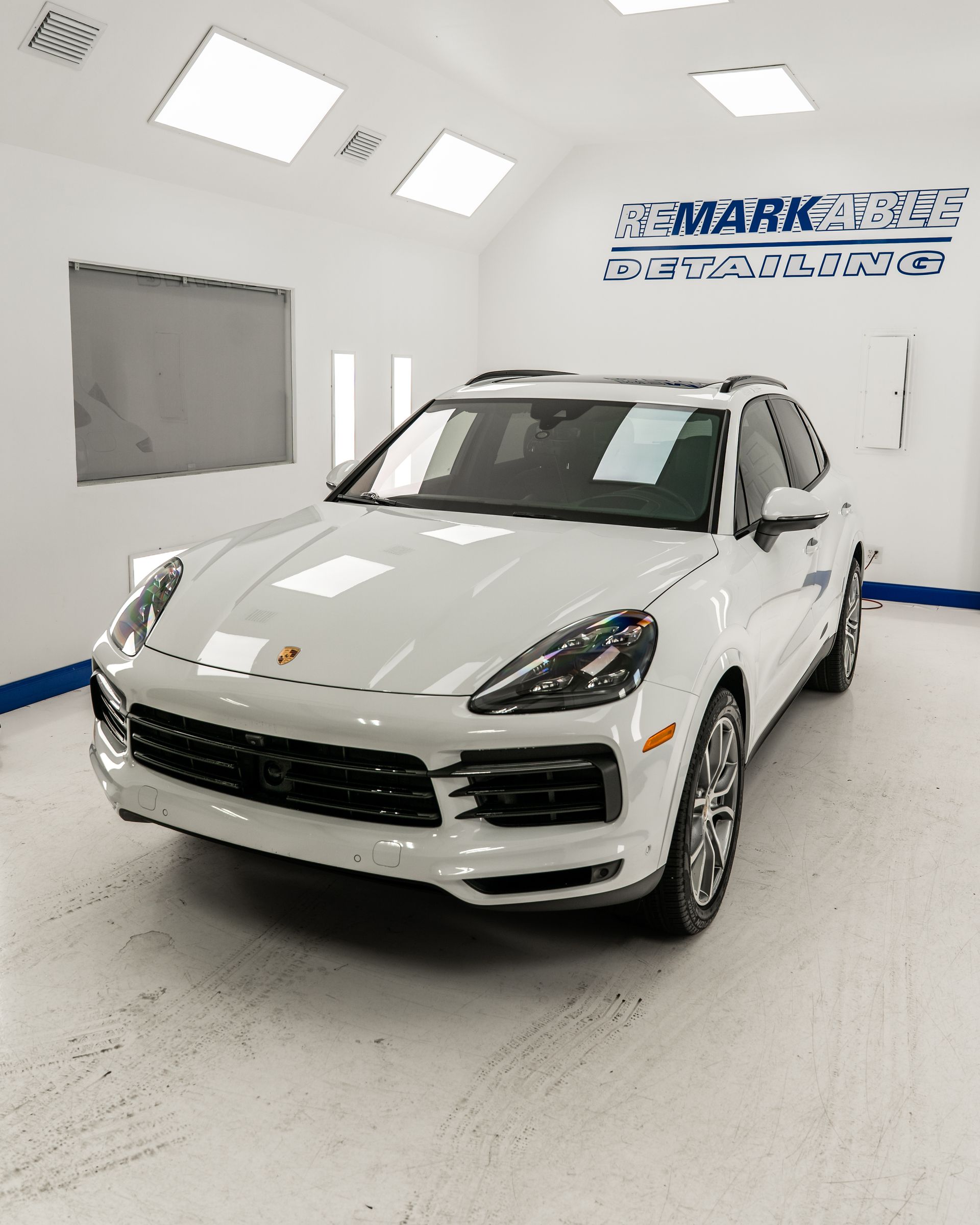 White Porsche SUV in a bright showroom with Mark Motors sign on the wall.