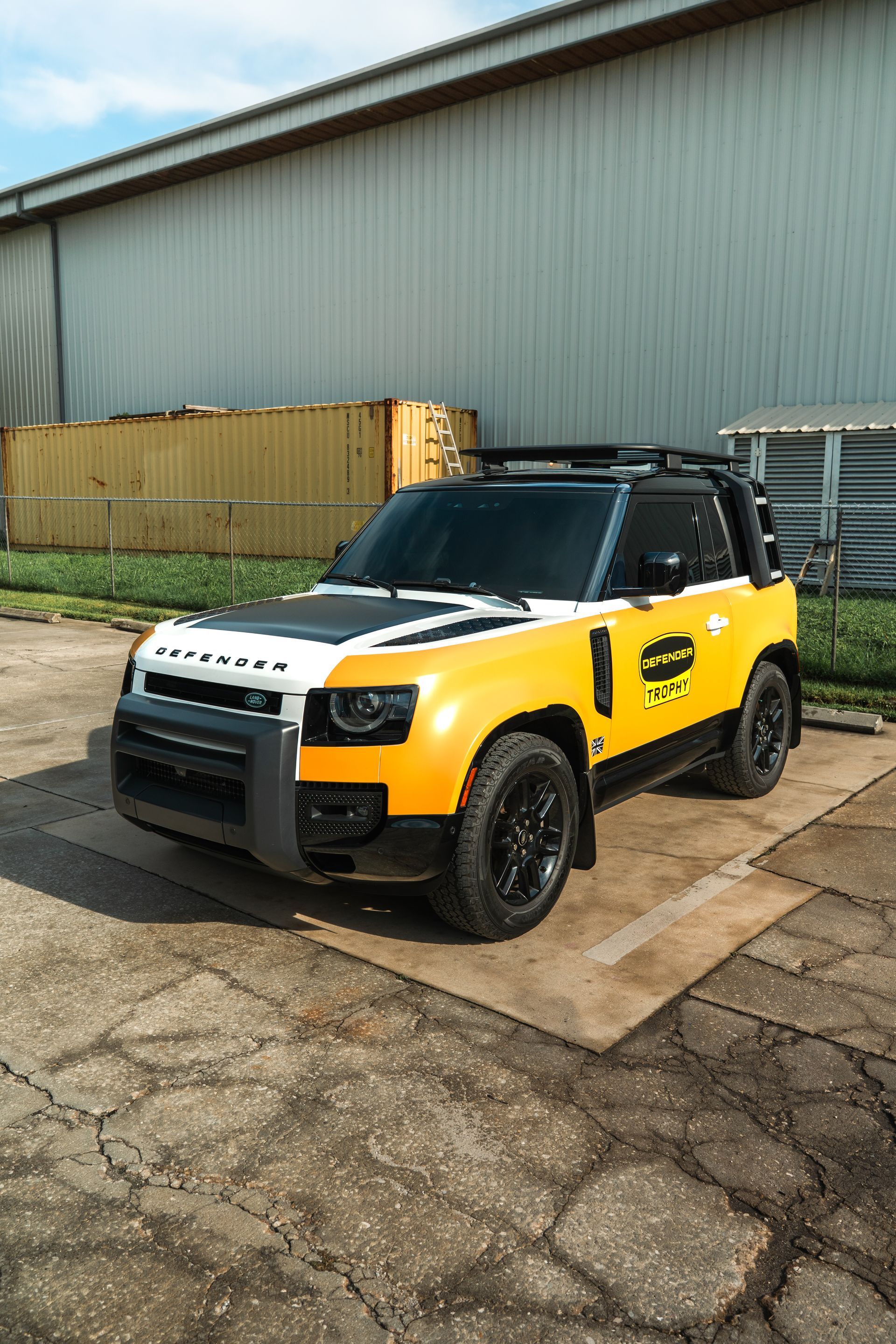 Yellow off-road SUV parked on cracked pavement beside a warehouse.