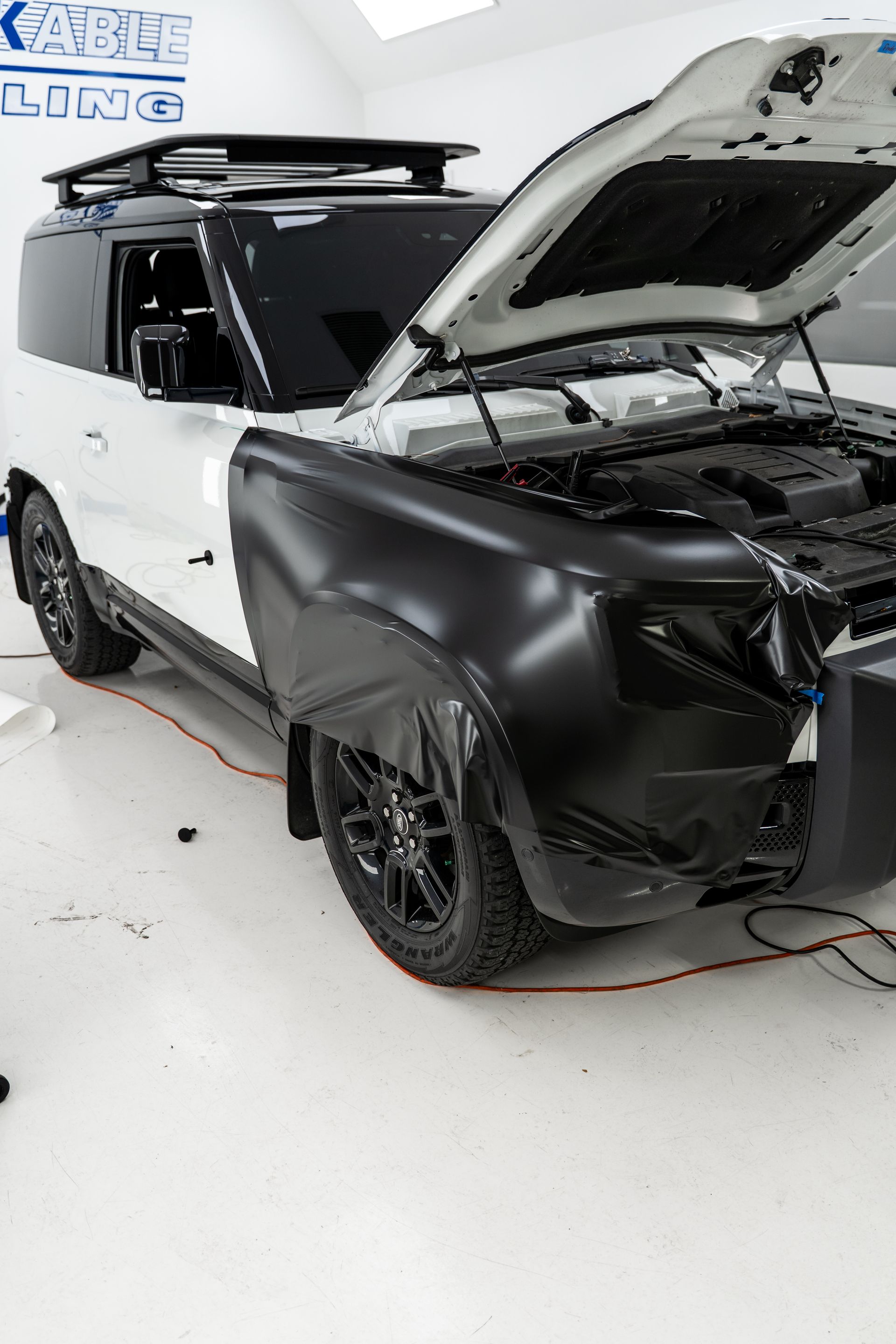 Black-and-white SUV with hood open in an auto shop, showing front-end repair work