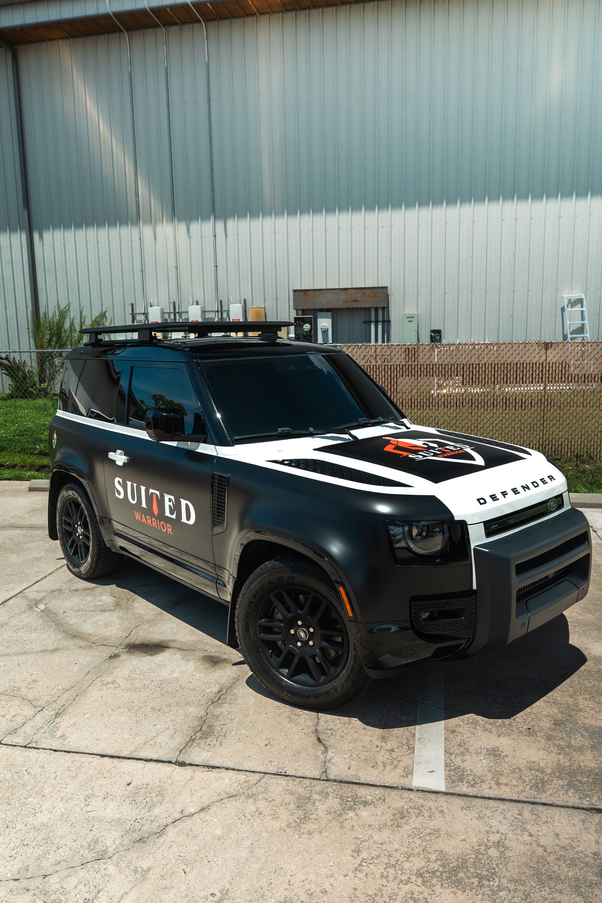 Black police-style SUV parked outside a metal building on a concrete lot
