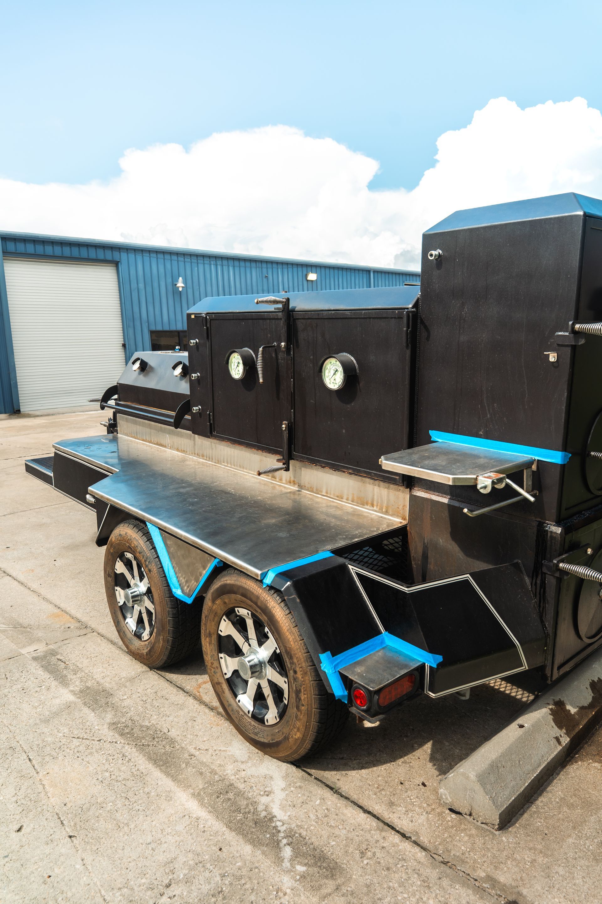 Black trailer with blue trim and tan wooden deck parked beside a blue building