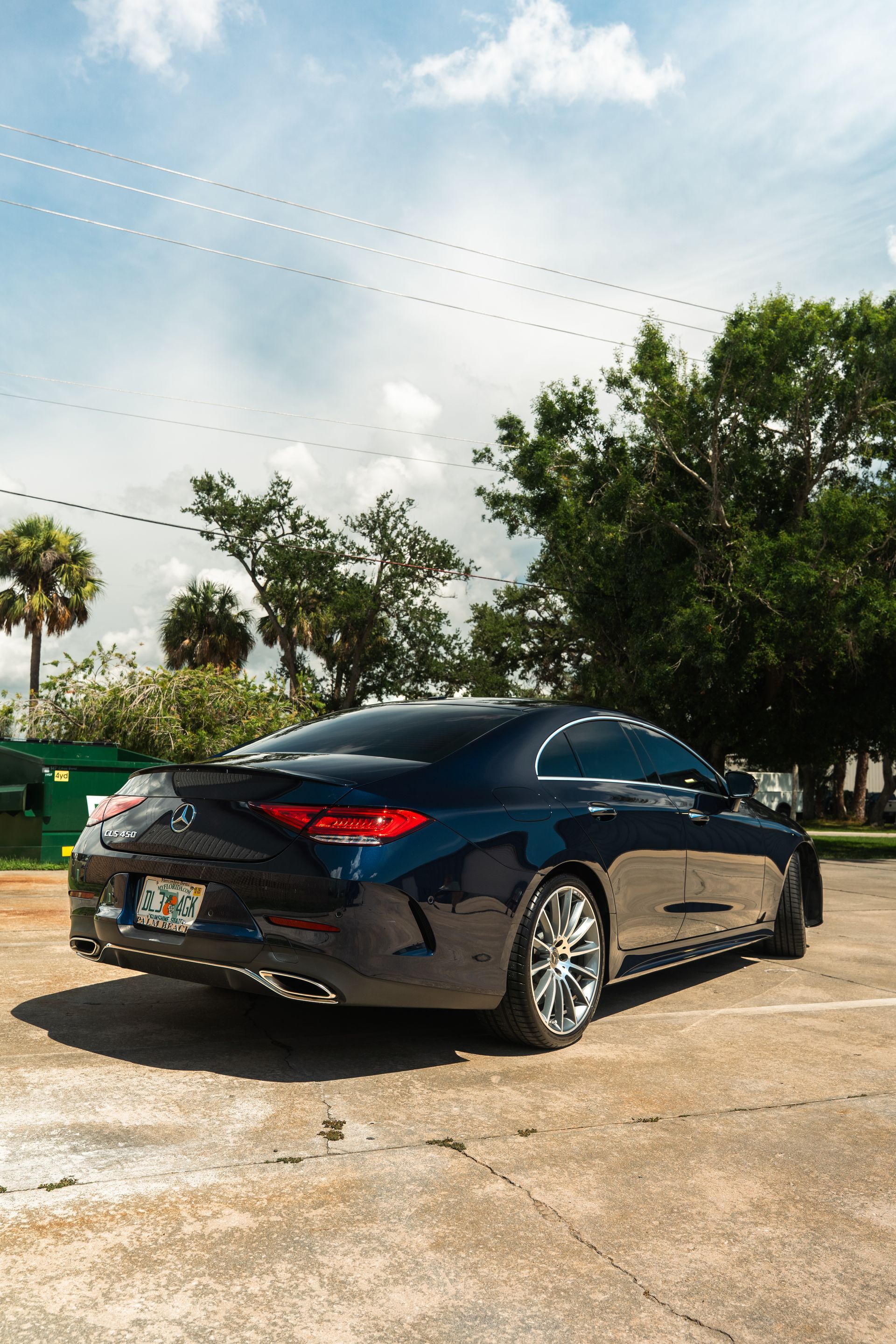 Dark blue coupe parked on a sunny concrete lot with trees and sky in the background