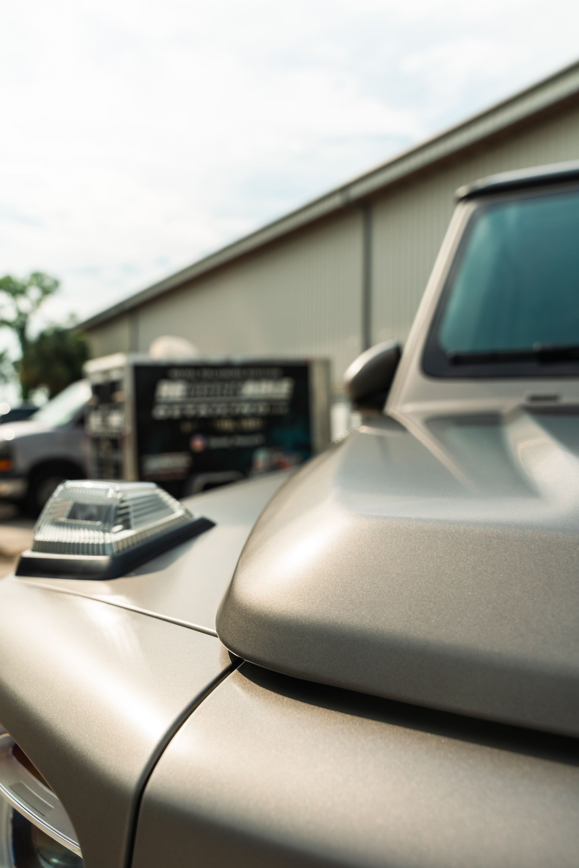 Close-up of a beige car hood with a raised hood scoop, parked outside a building.