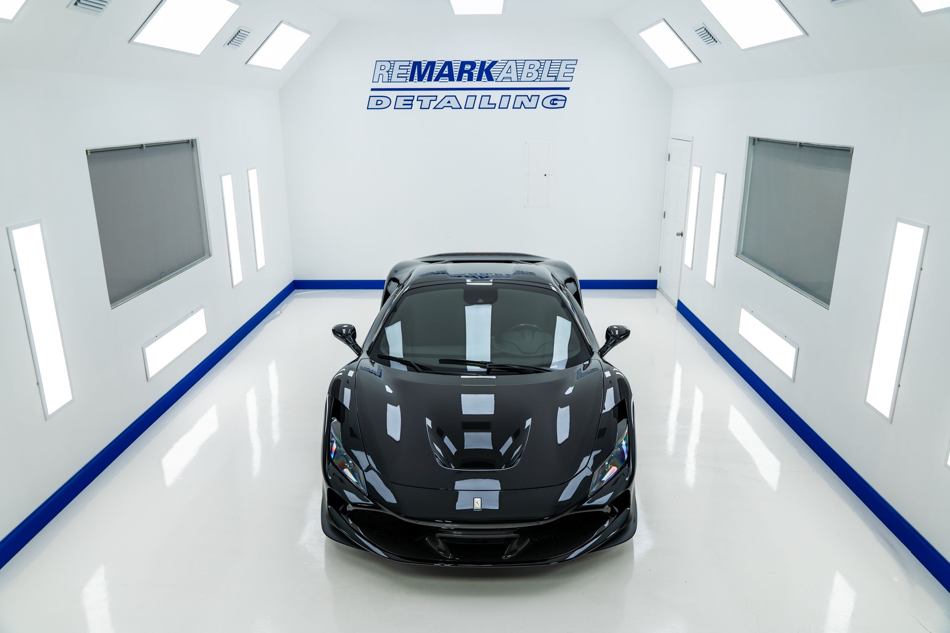 Black sports car in a white showroom with bright lights and blue trim lines