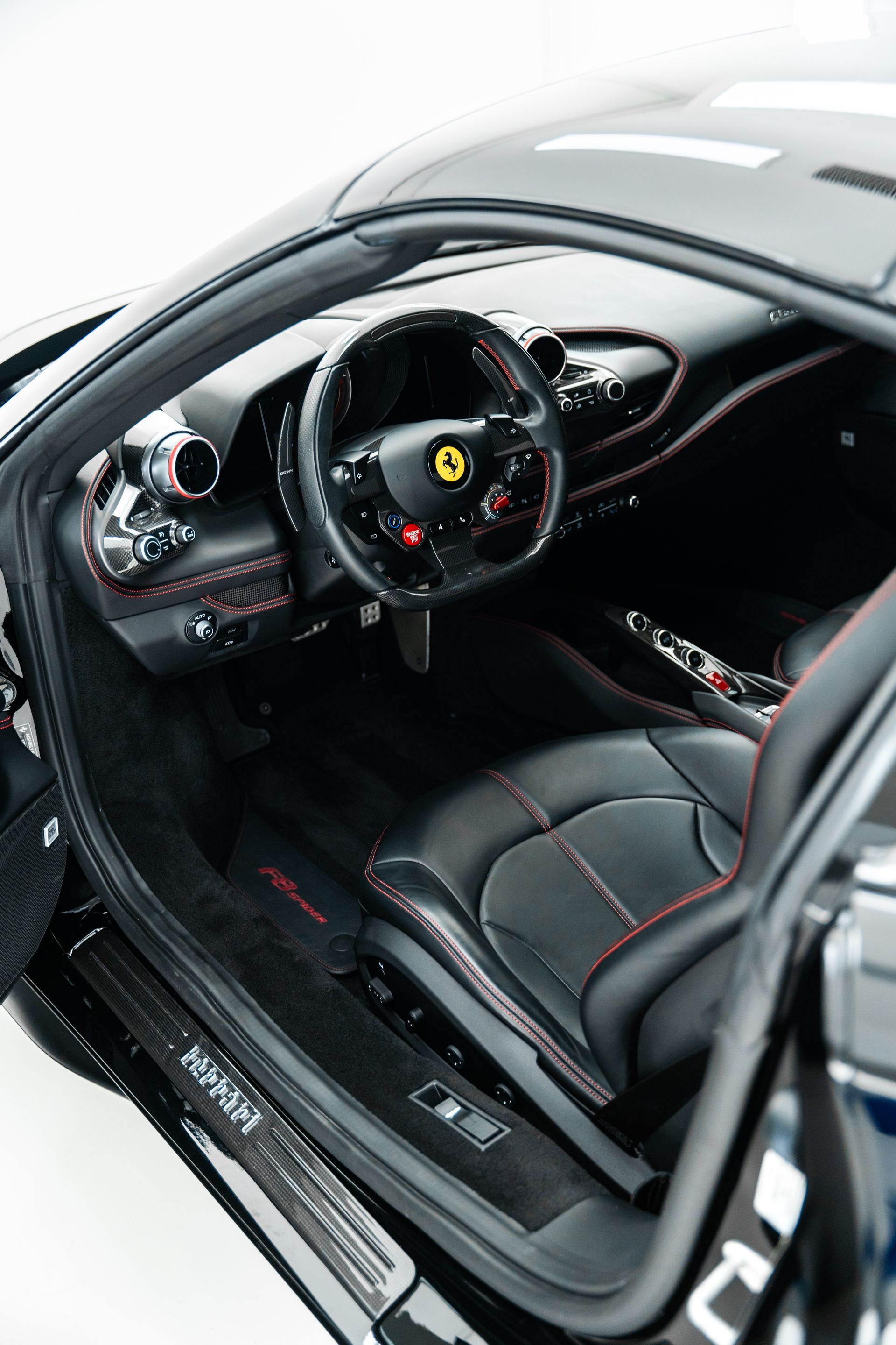 Ferrari sports car interior with black leather seats, red stitching, and a steering wheel visible from the open door