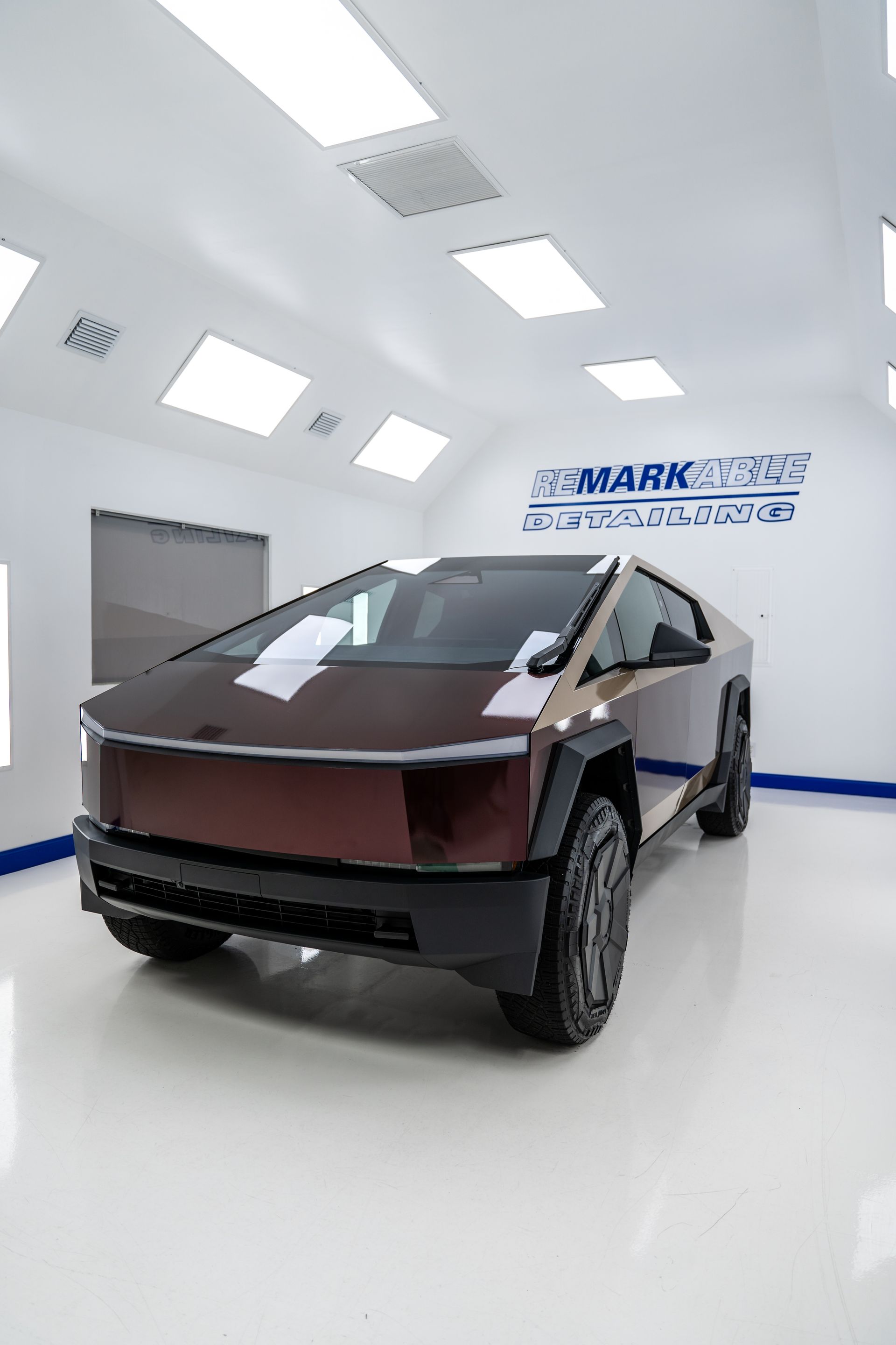 Futuristic brown Tesla Cybertruck in a white showroom with bright ceiling lights